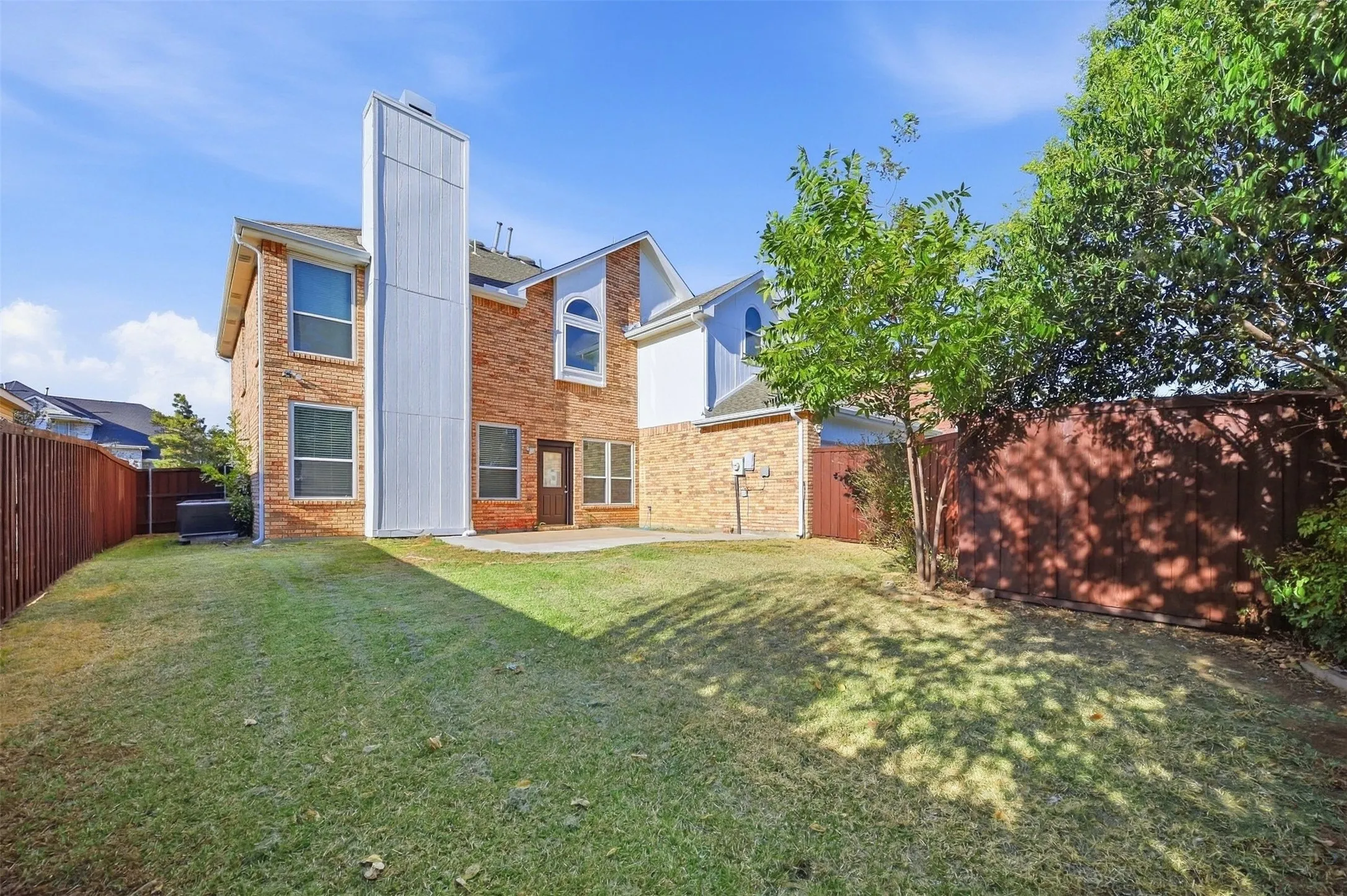 Brick exterior with a prominent vertical chimney structure, multiple windows, and a ground-level patio