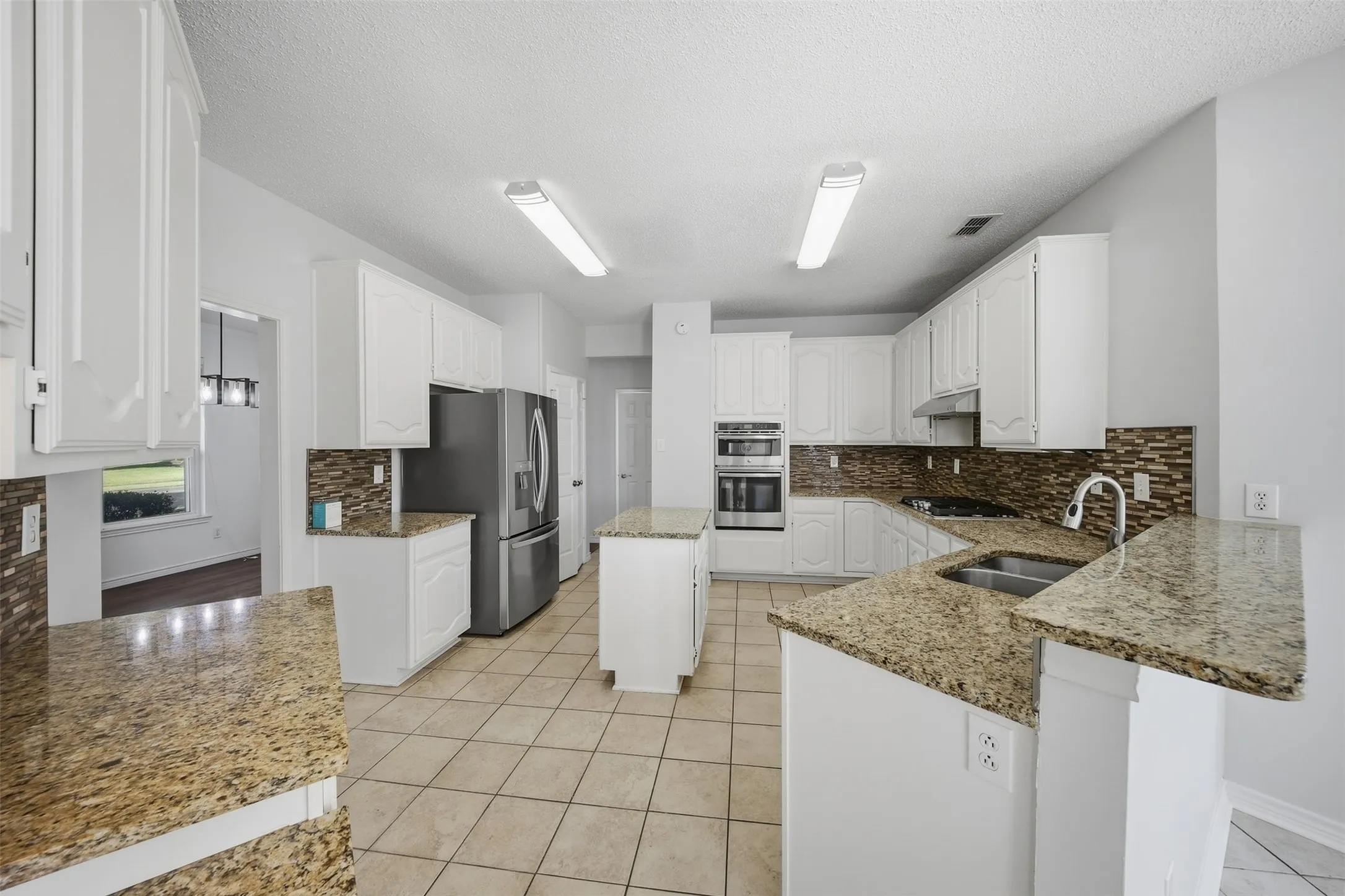 Spacious kitchen featuring extensive granite countertops, white cabinetry, tile flooring, a tile backsplash, and stainless steel appliances