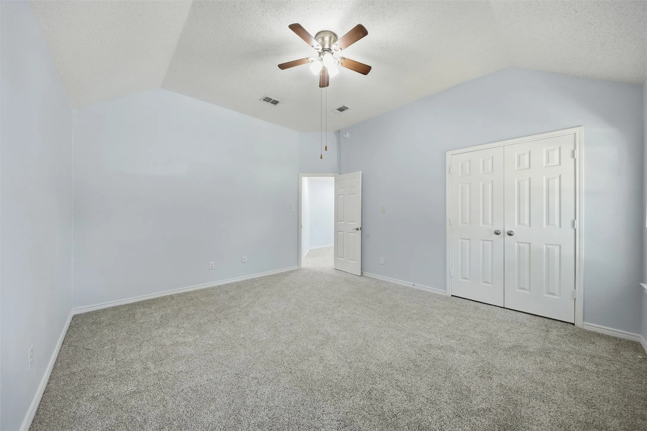 Vaulted ceiling with a ceiling fan, light gray carpeting, and white paneled bi-fold closet doors