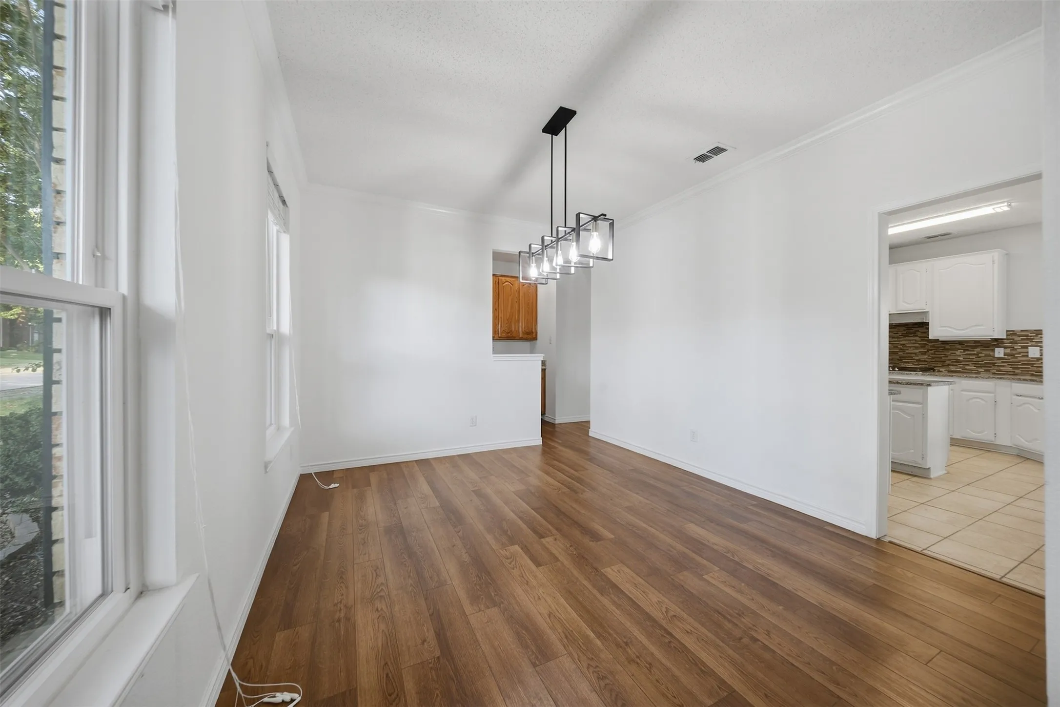 Wood-finish flooring, white walls with crown molding, and a modern rectangular chandelier