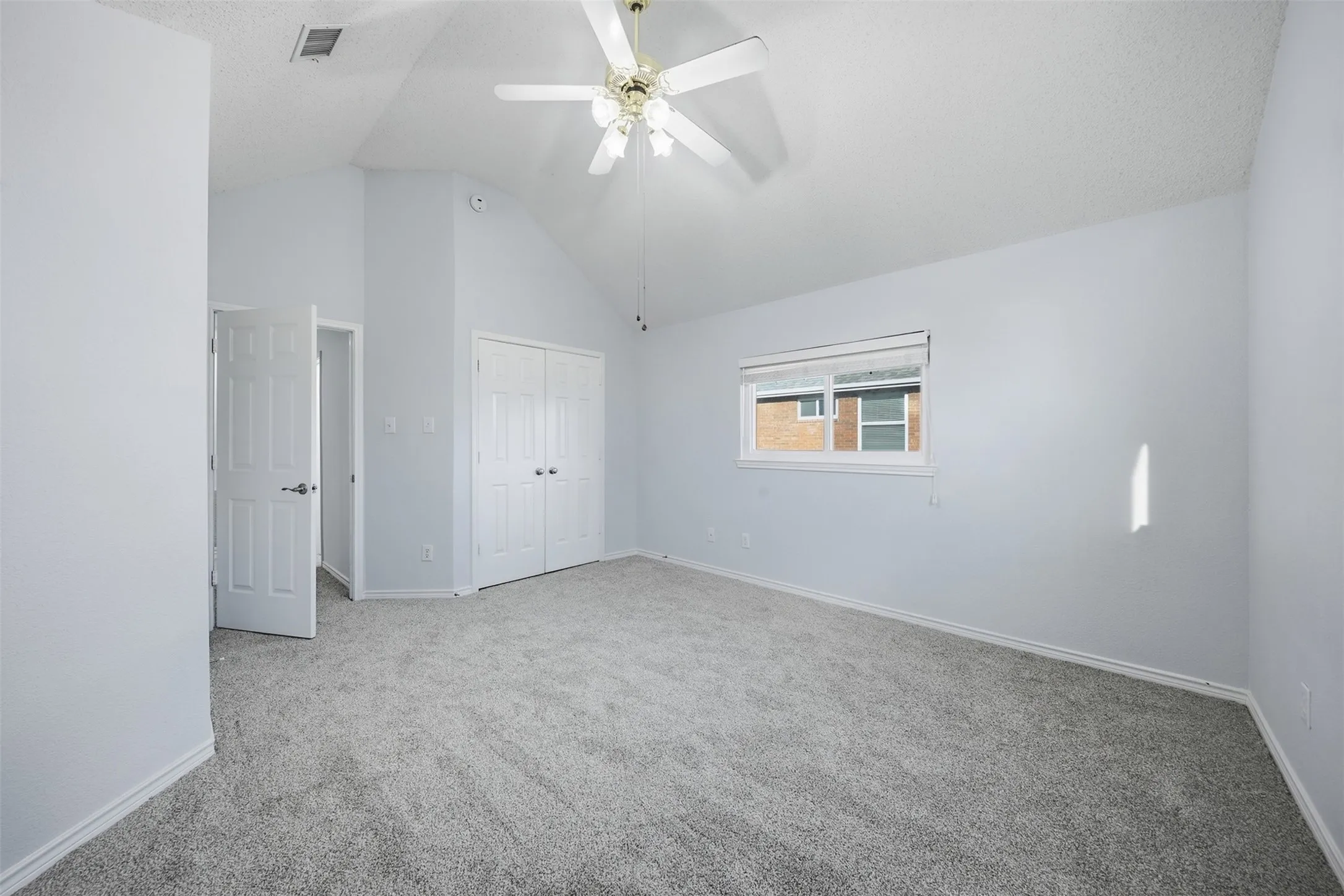 Vaulted ceiling, ceiling fan, bi-fold closet doors, window with roller shade, and gray carpet flooring