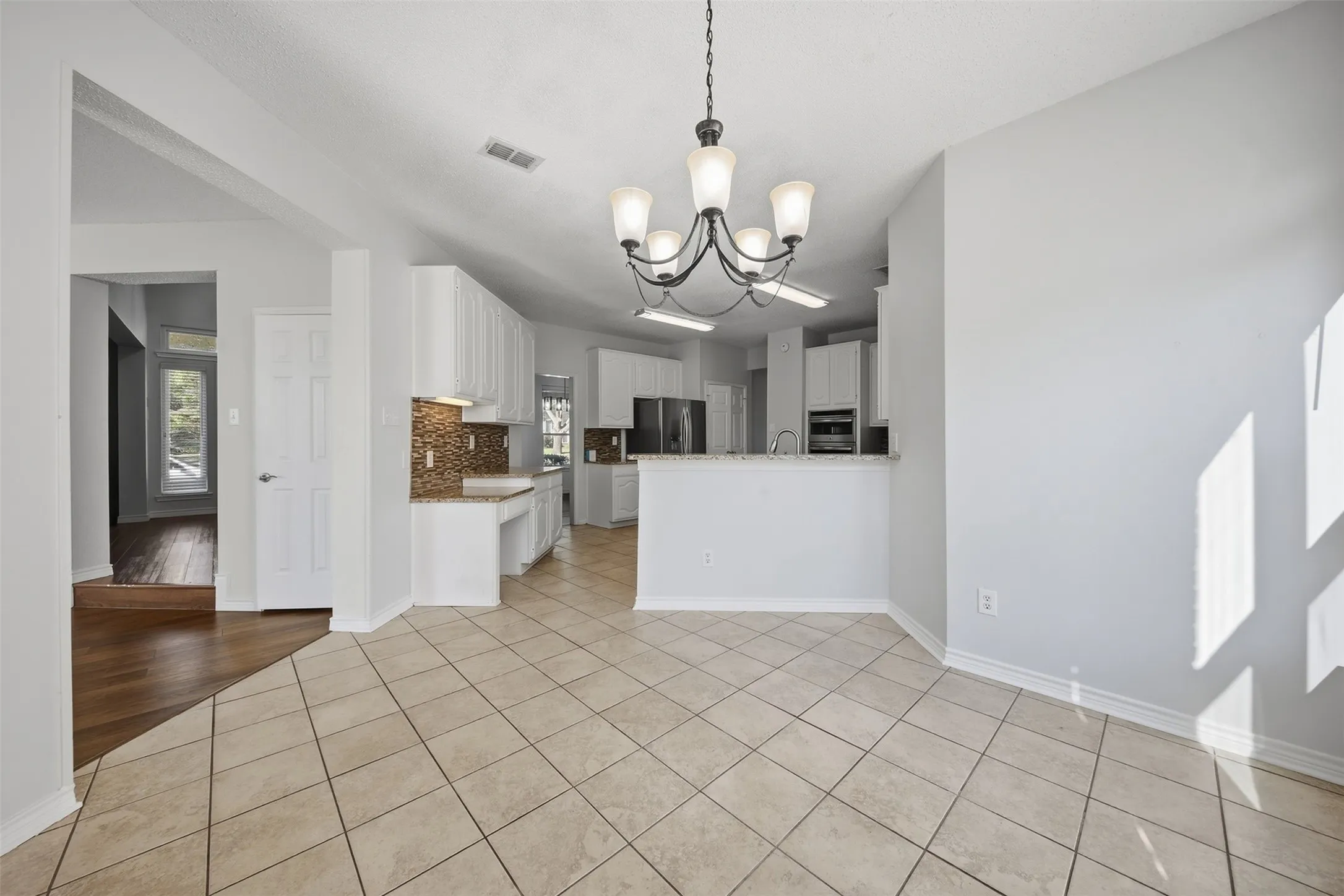 Vaulted ceiling with chandelier, tile flooring, wood-finish flooring, white cabinetry, and a mosaic tile backsplash