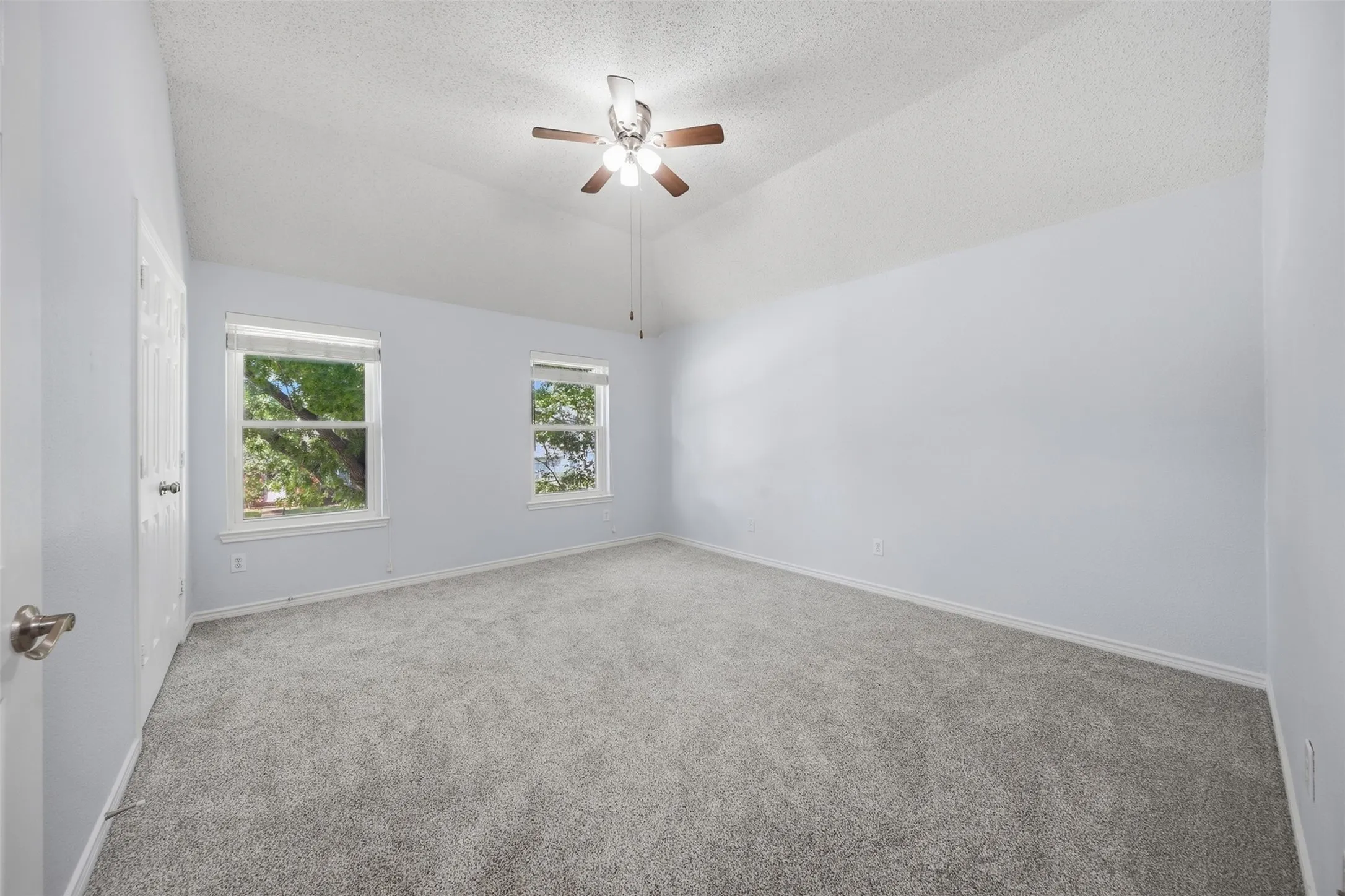 Vaulted ceiling with a ceiling fan, two double-hung windows, and wall-to-wall carpeting