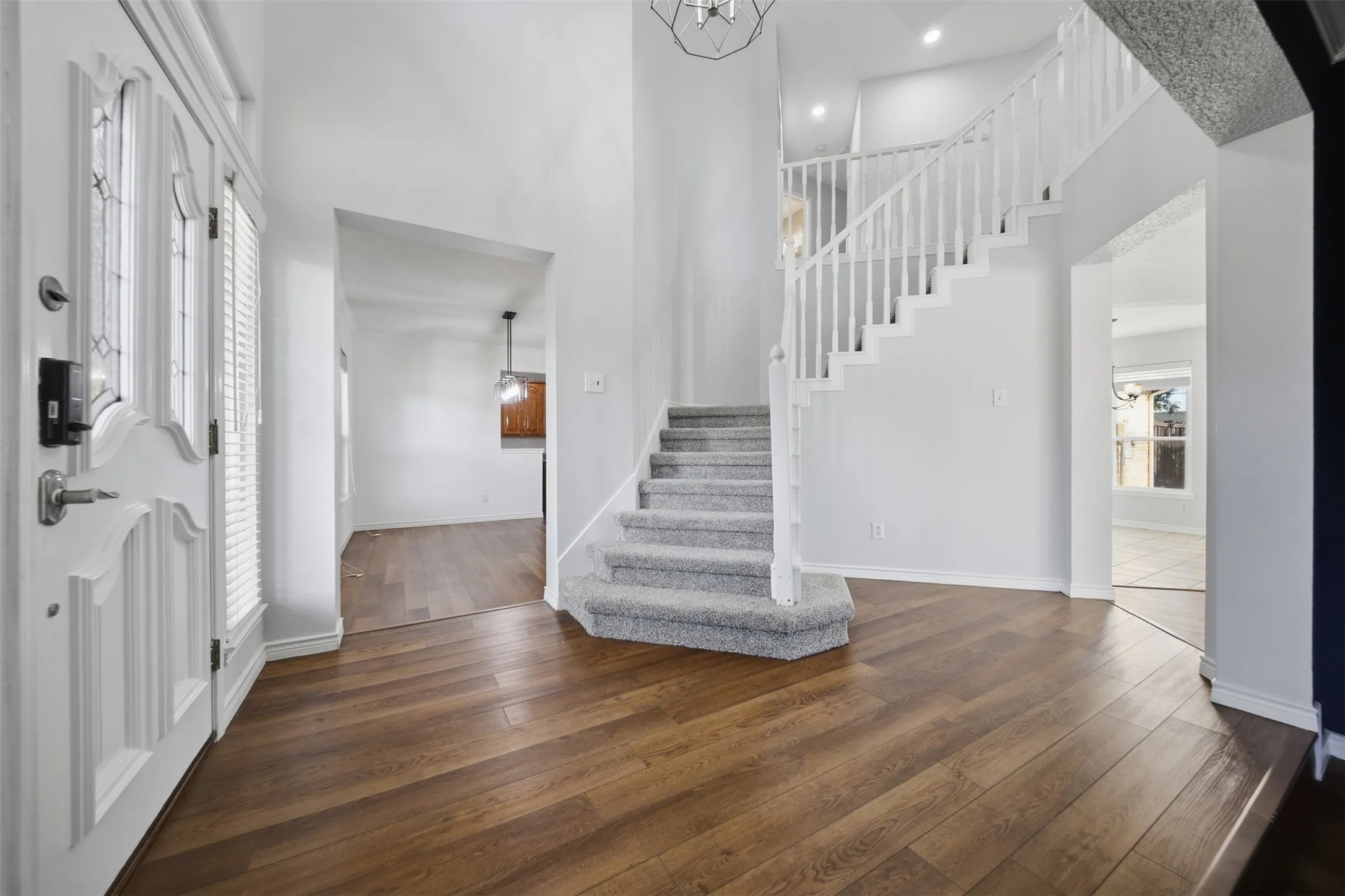 Entryway featuring wood-finish flooring, a carpeted staircase with white balusters, a double front door with decorative glass, and a high ceiling
