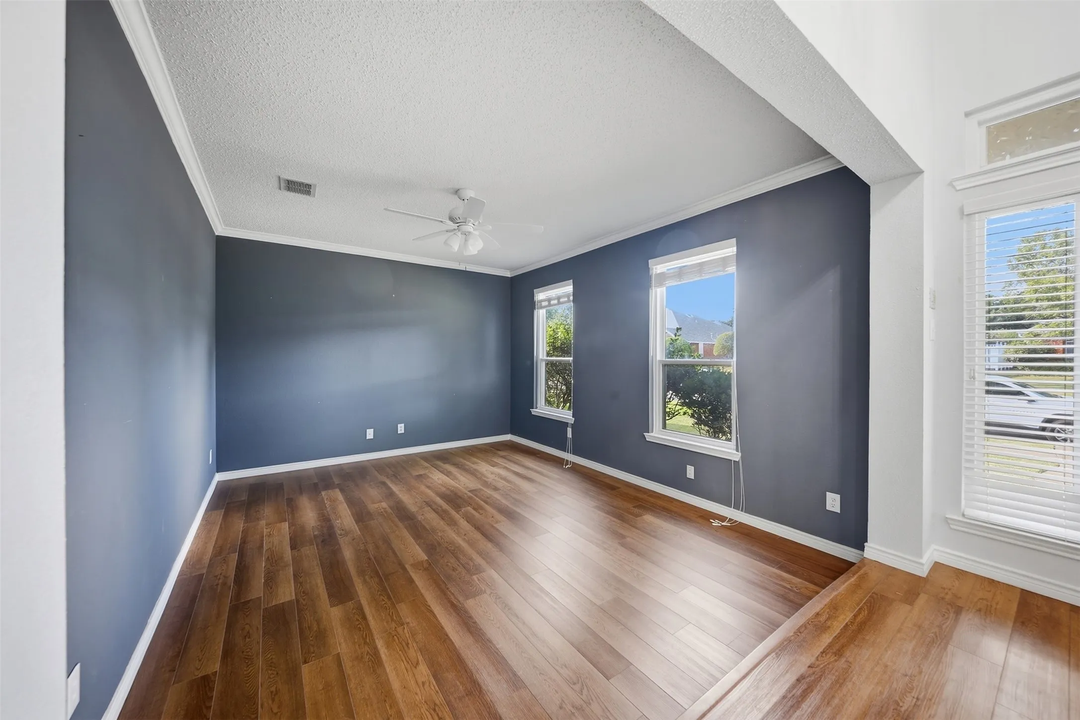 Wood-finish flooring, crown molding, white ceiling fan, and multiple windows