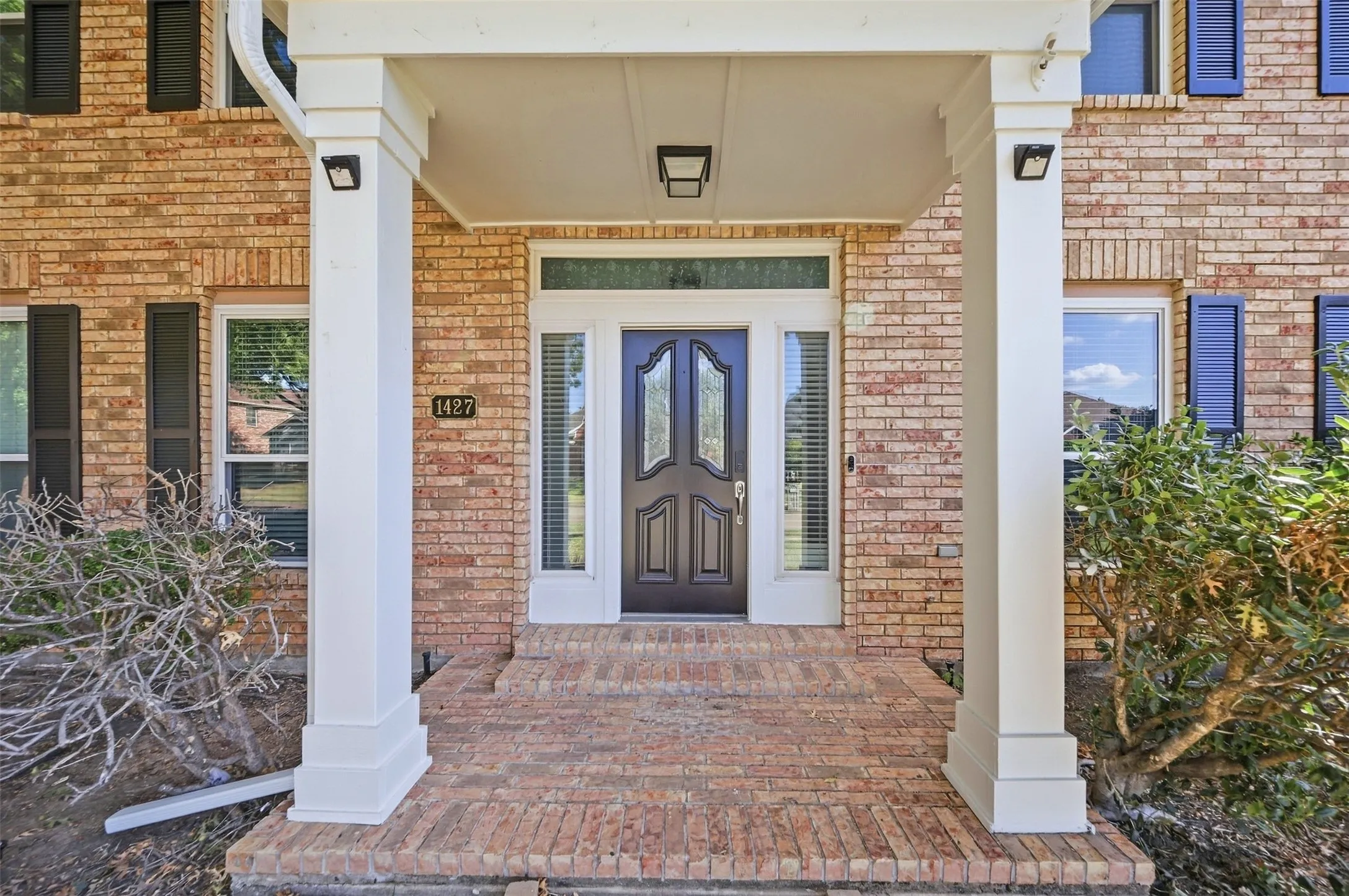 Brick exterior featuring a covered entry, white columns, a dark wood-finish door with decorative glass, and side lites with transoms