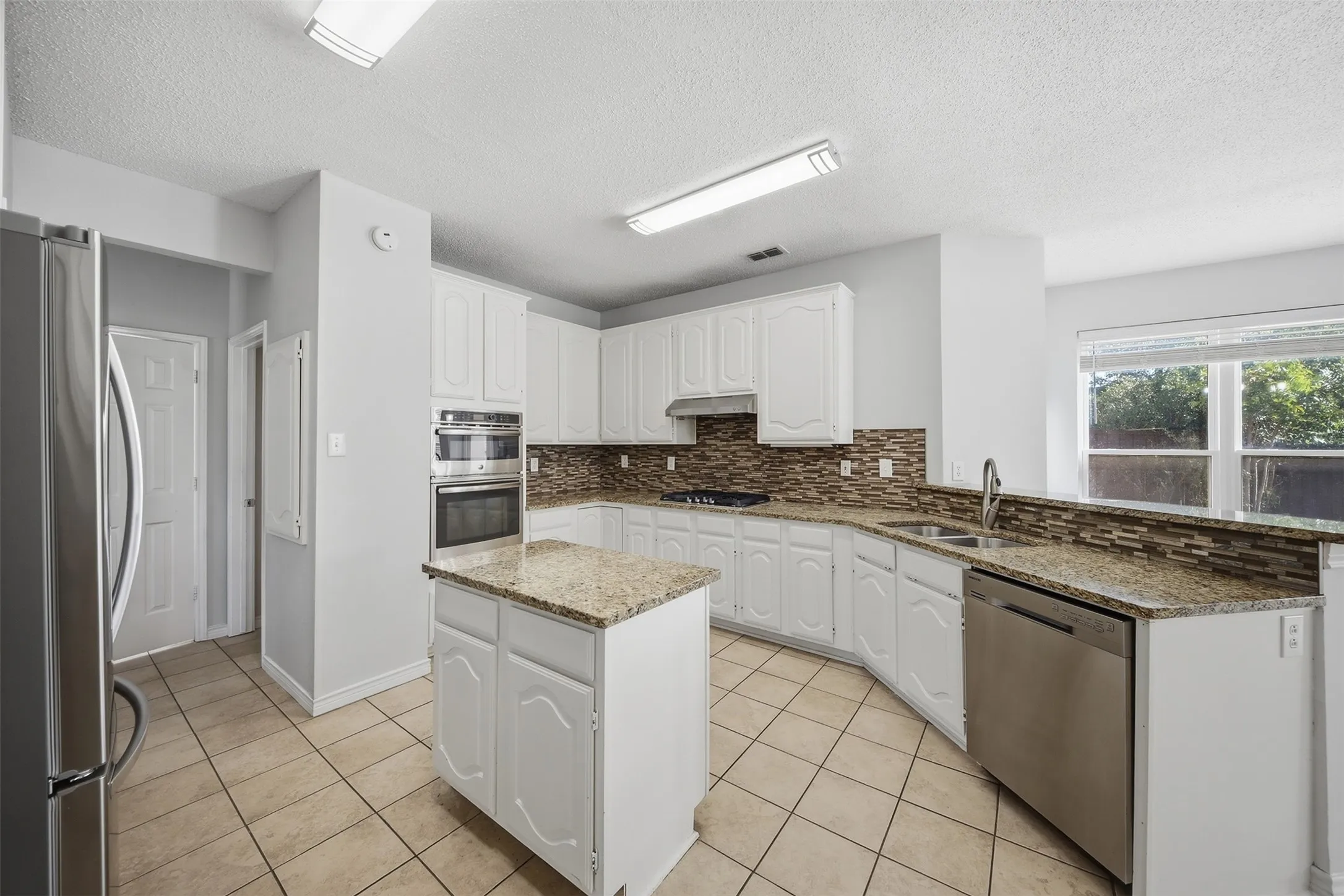 Kitchen featuring an island, white cabinetry, integrated stainless steel appliances, tile backsplash, and light-toned countertops