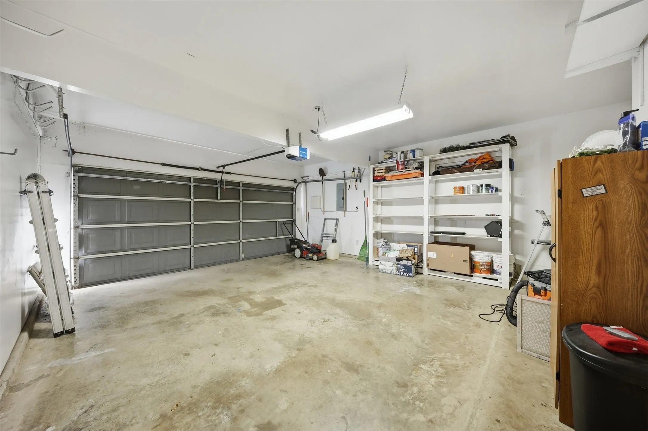 Concrete flooring garage with an overhead door, white walls, and fluorescent lighting