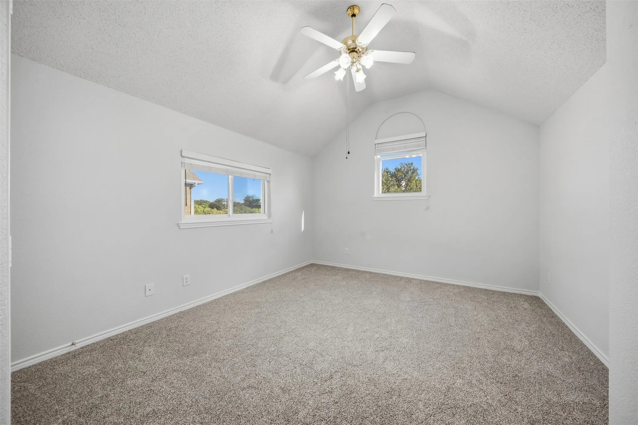 Vaulted ceiling with a ceiling fan, arched window, standard window, and neutral carpeting