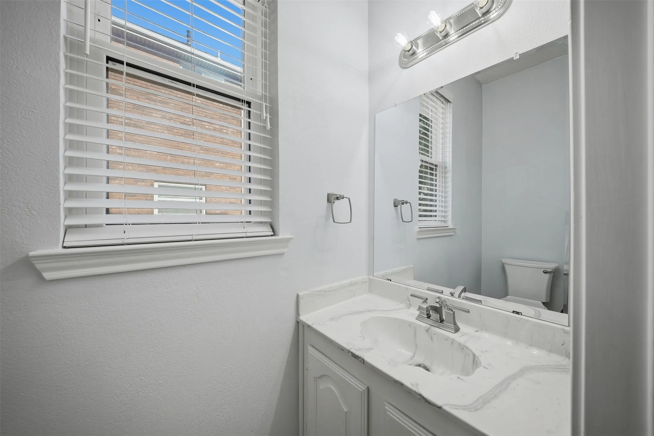 White vanity with paneled cabinetry, integrated sink, and a marbled countertop
