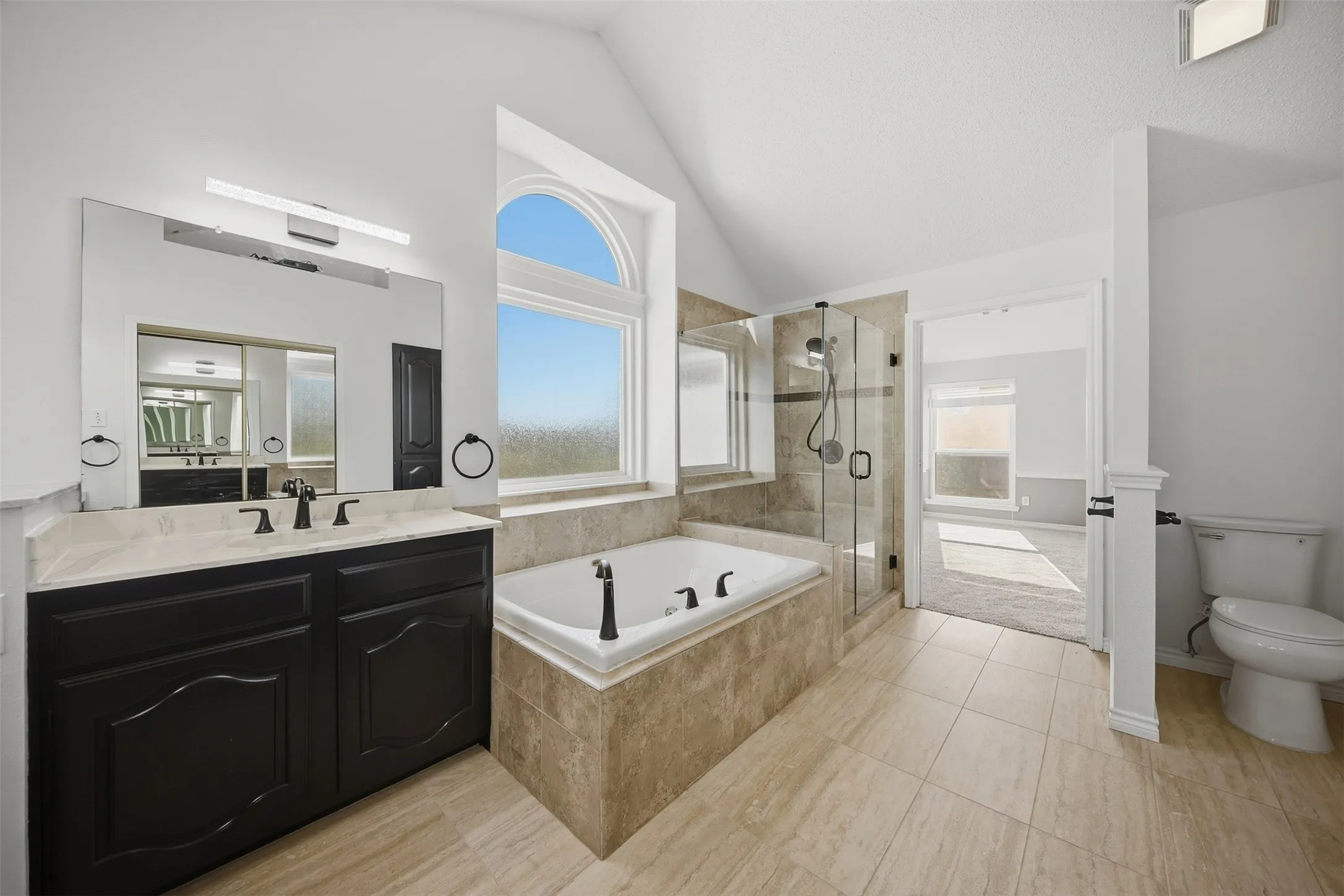 Spacious bathroom featuring a built-in soaking tub, a separate glass-enclosed shower, a double vanity with ample storage, and neutral-toned tile flooring
