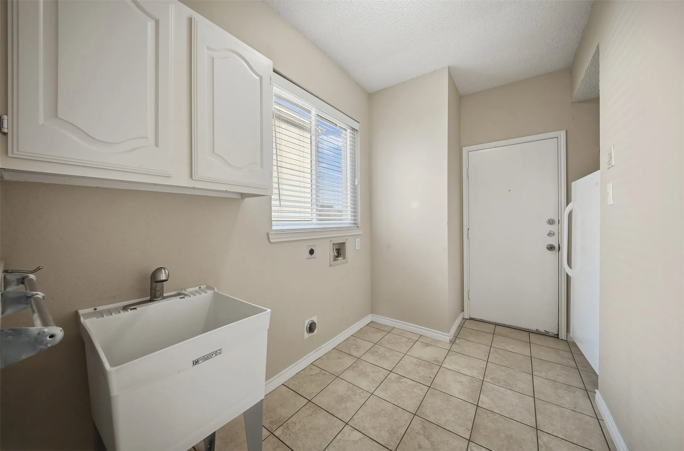 White cabinetry, utility sink, large window, tile flooring, and integrated laundry connections