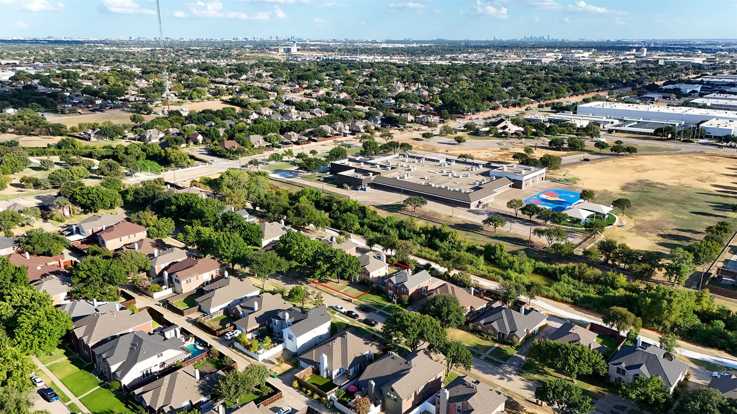 Expansive aerial perspective showcasing a residential neighborhood with mature trees, commercial structures, and open green spaces