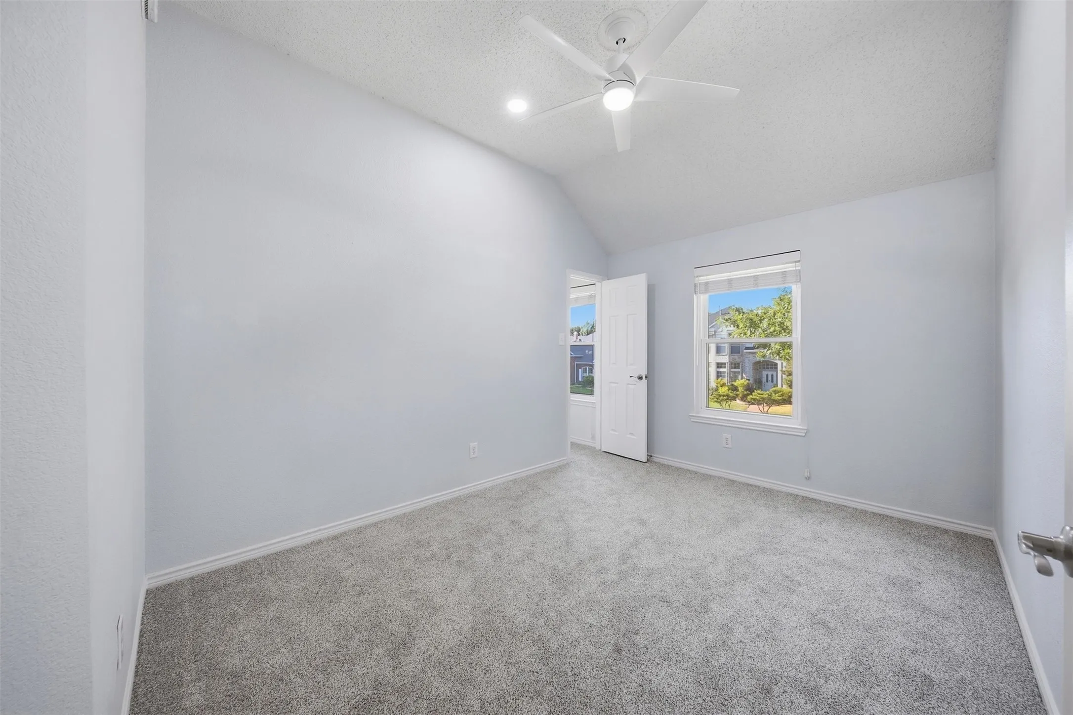 Vaulted ceiling, recessed lighting, ceiling fan, white trim window, and gray carpeting