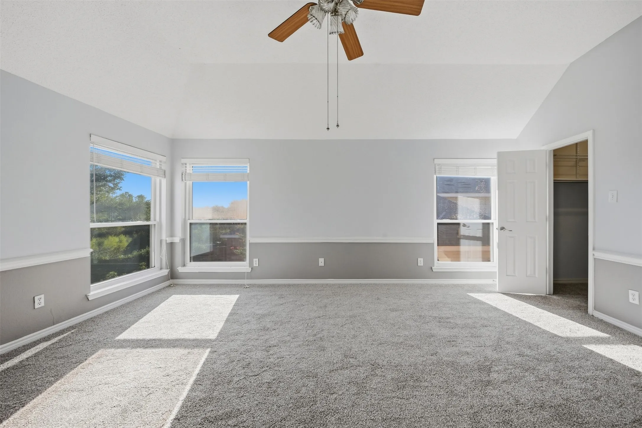Vaulted ceilings, a ceiling fan, gray carpet flooring, and multiple windows with white trim