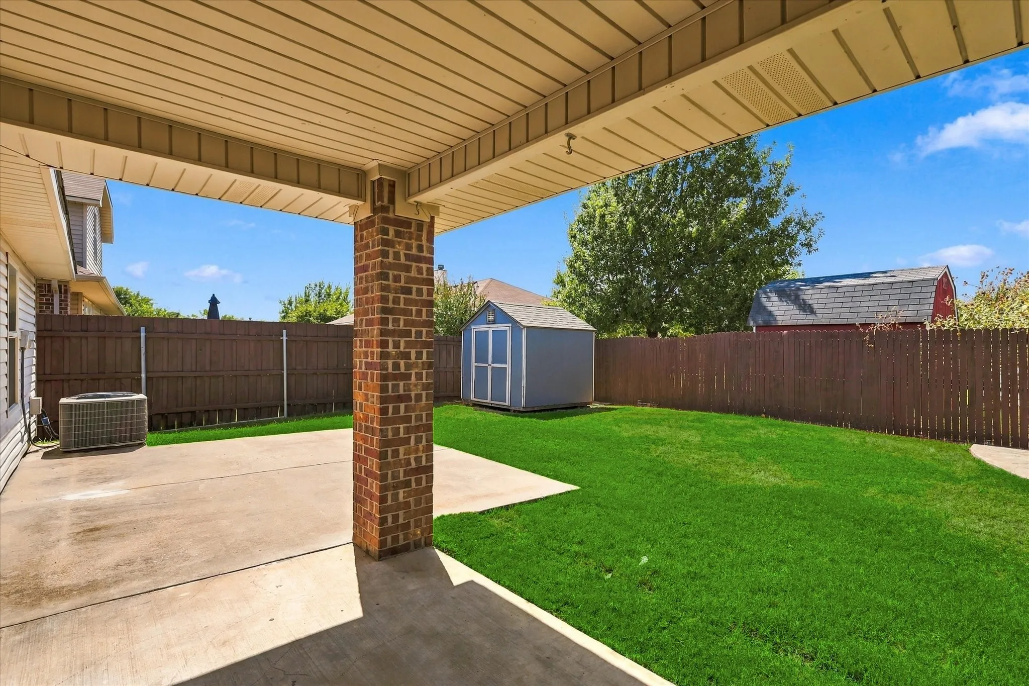 Covered patio with a brick pillar, concrete patio area, and expansive green lawn