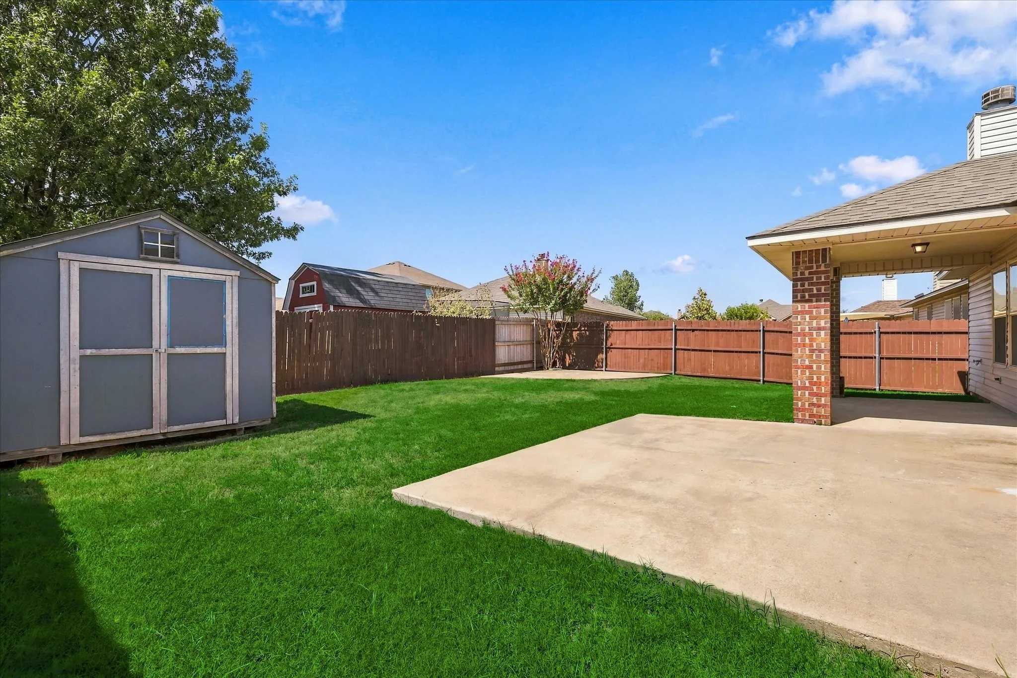 Expansive fenced backyard featuring a storage shed, concrete patio, and lush lawn
