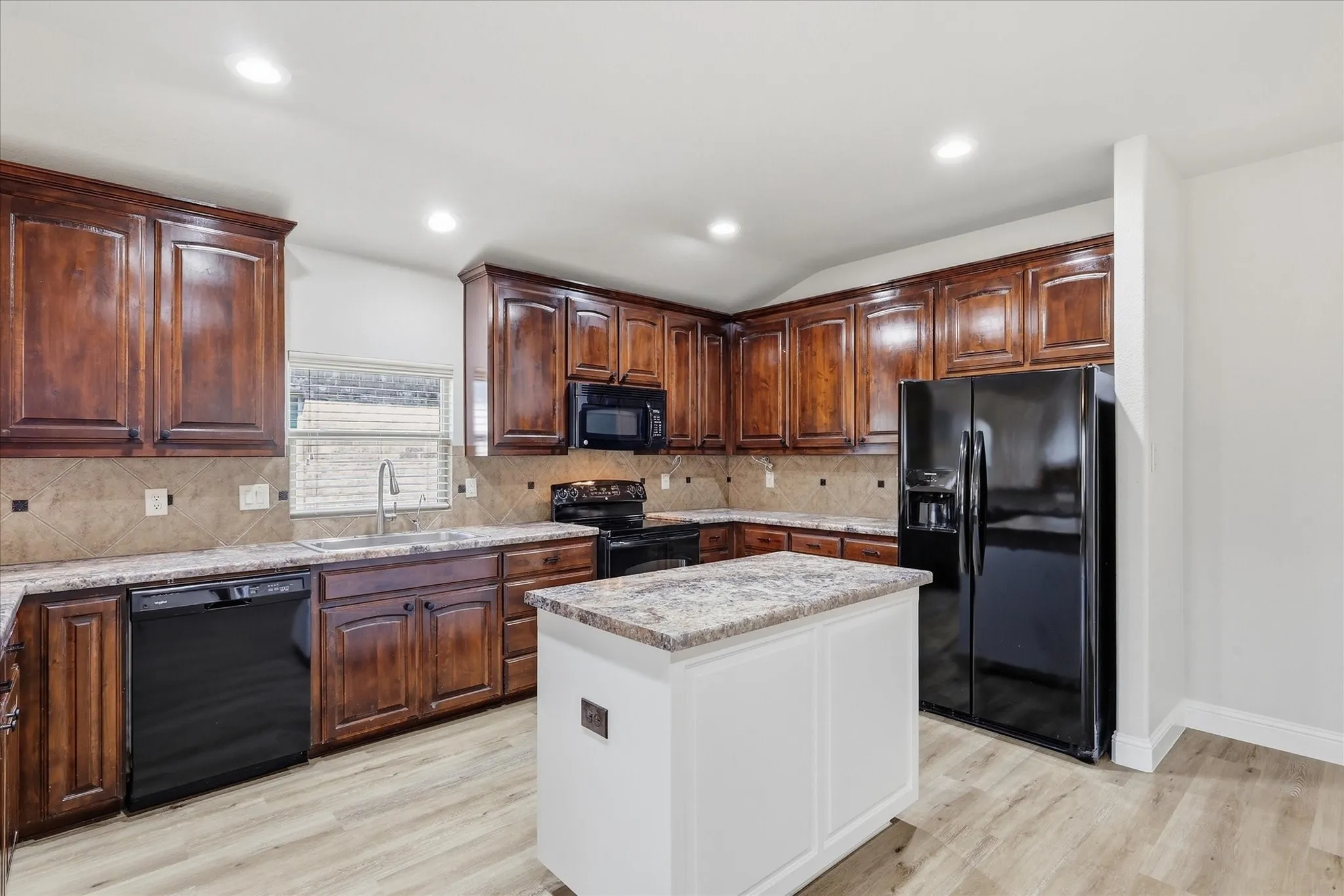 Kitchen featuring wood-finish cabinetry, light-toned countertops, a central island, and black appliances