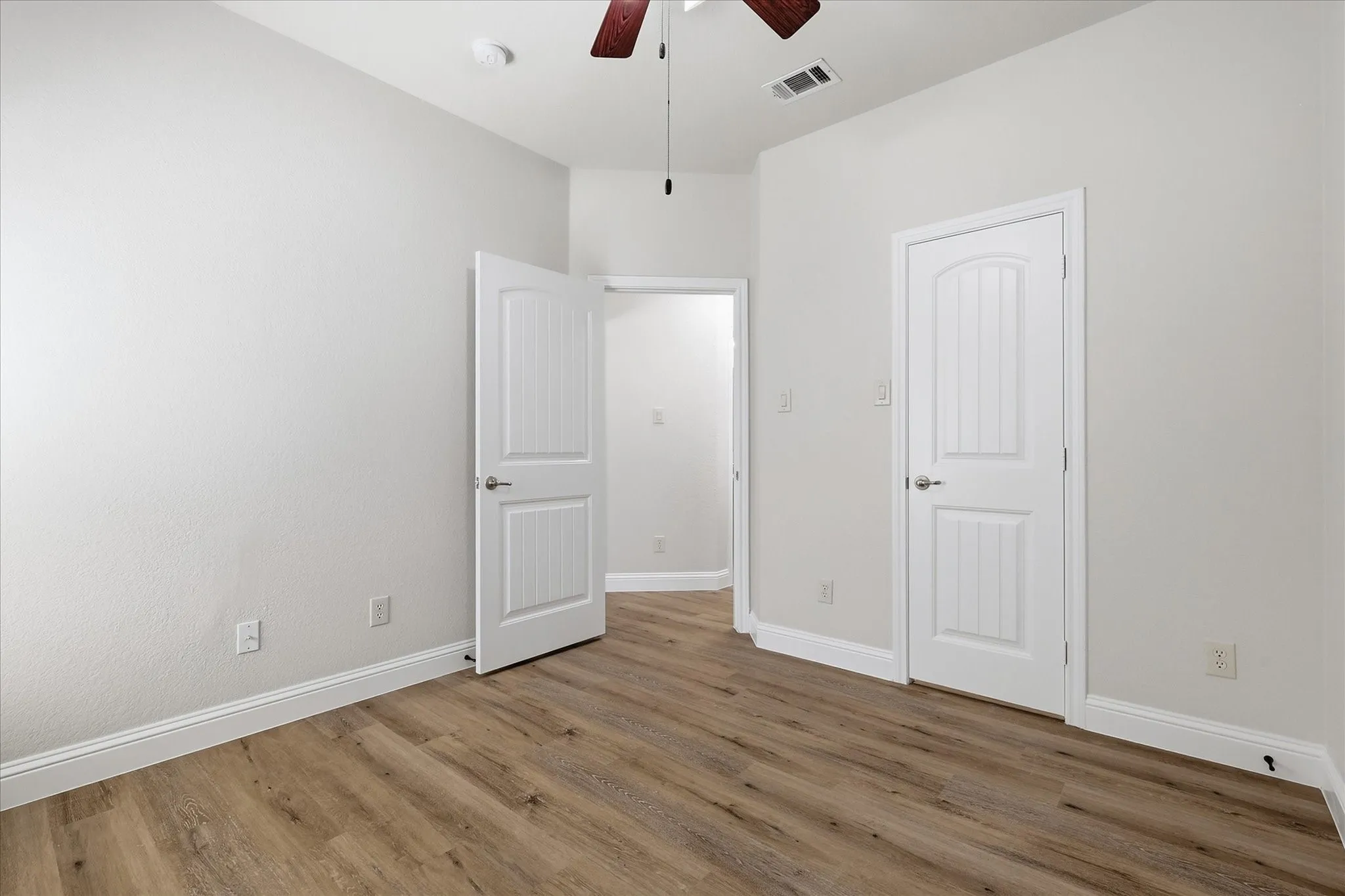 Wood-finish flooring, white trim, white paneled doors, and a ceiling fan