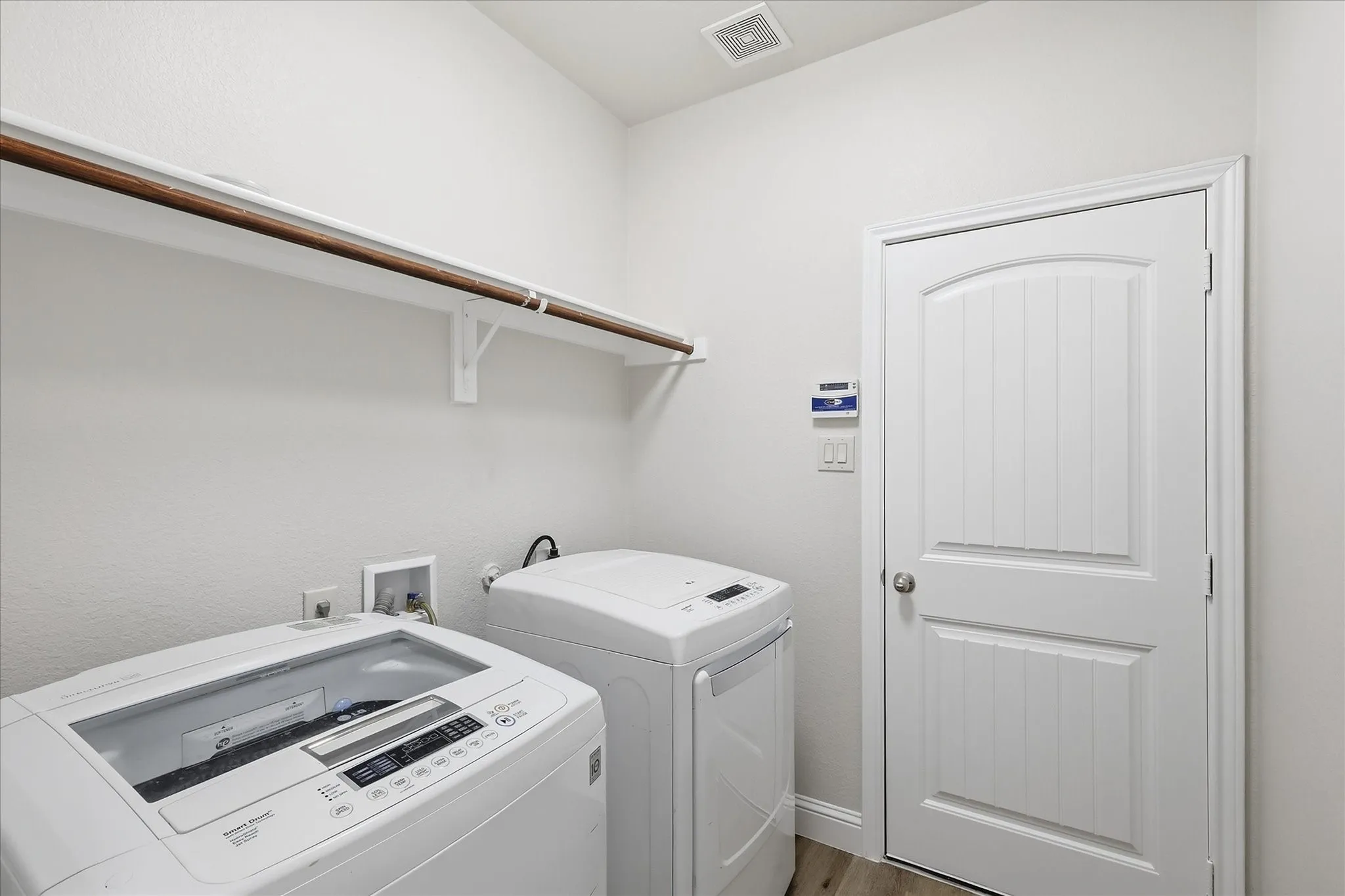 Laundry area featuring a wall-mounted shelving unit with a hanging rod, a white paneled door with an arched top, and light-toned flooring