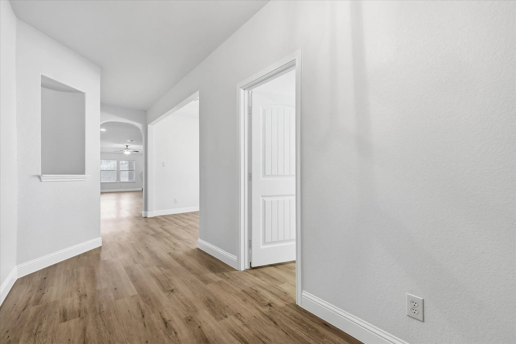 Hallway with wood-finish flooring, an arched doorway, and a built-in wall niche