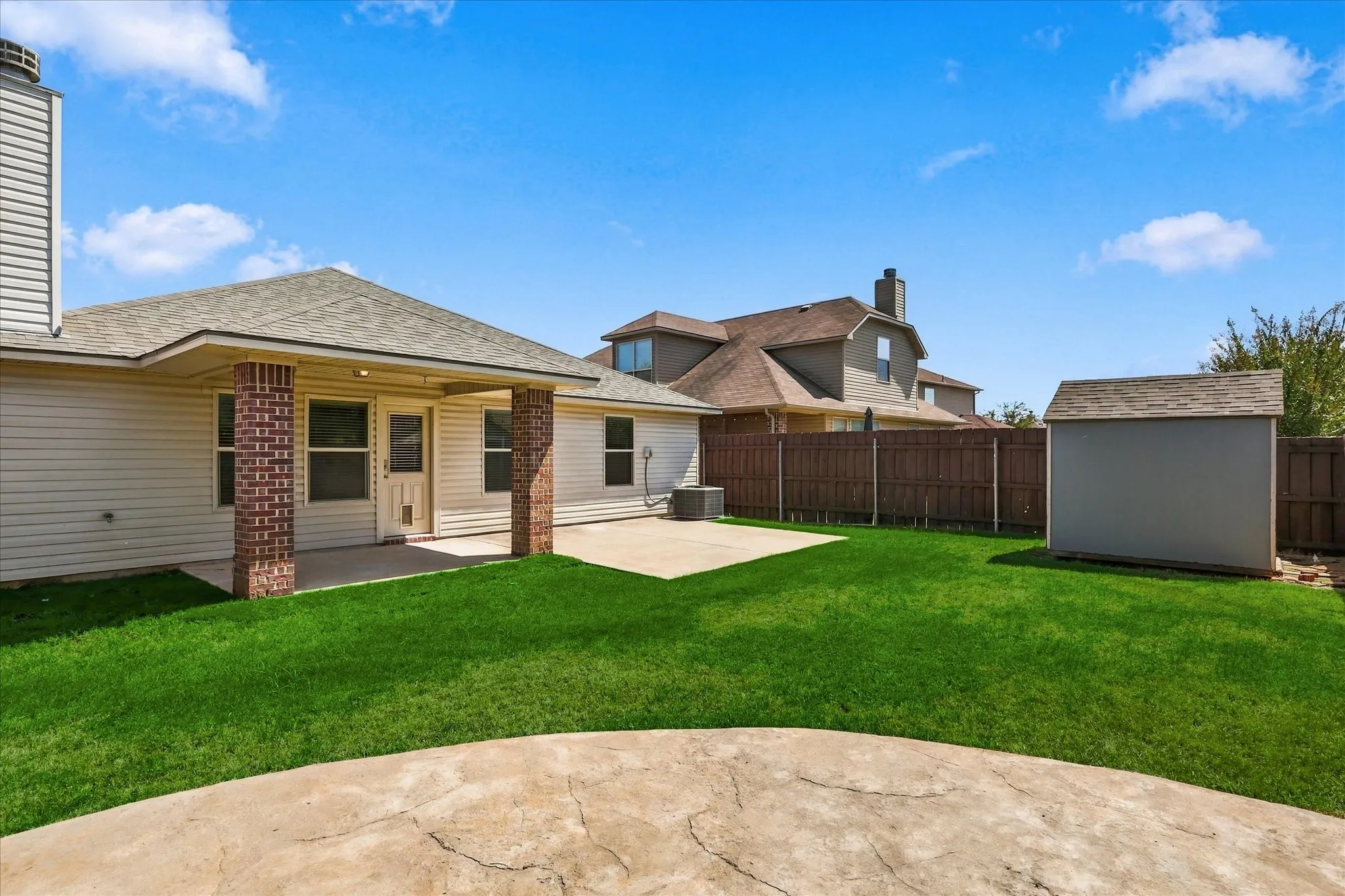 Expansive backyard featuring a manicured lawn, concrete patio, and a storage shed