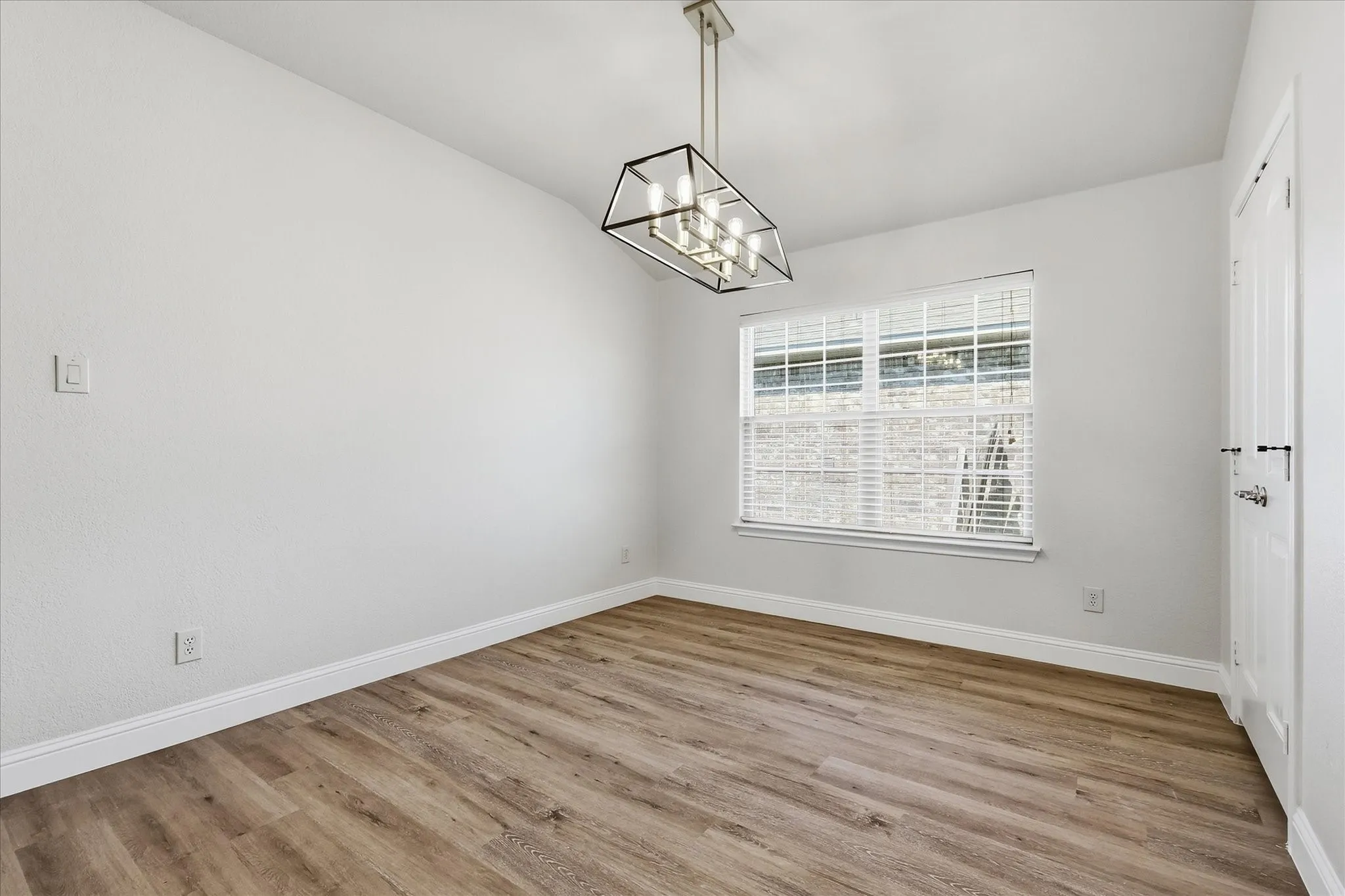 Wood-finish flooring with white baseboards, a suspended geometric chandelier, and a window with blinds