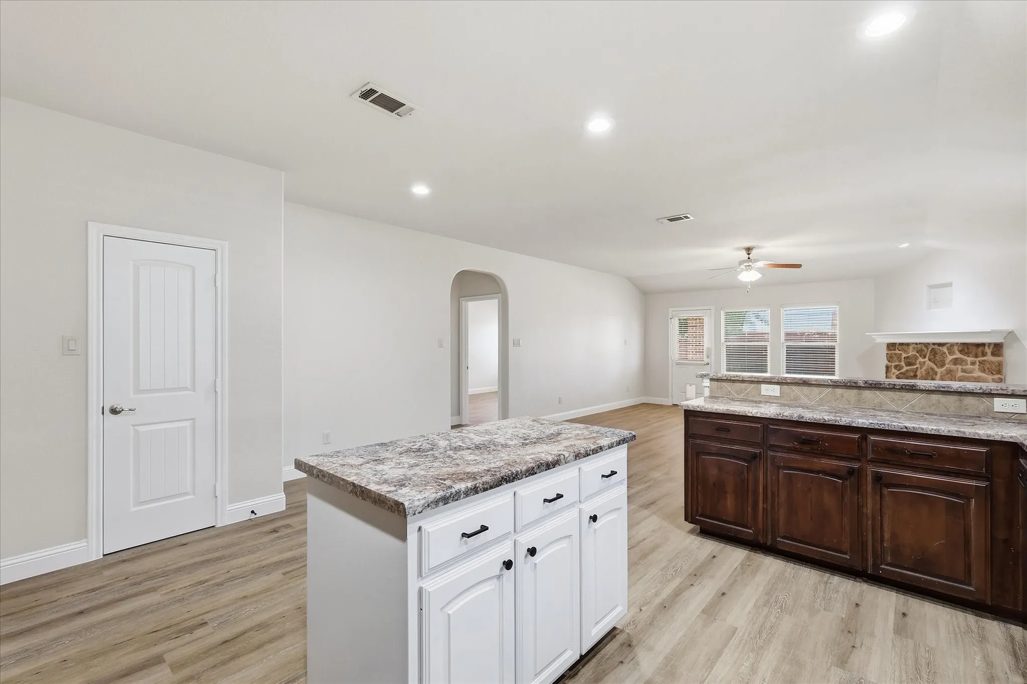 Wood-finish flooring throughout, kitchen island with cabinet storage, stone-look countertops, dark wood-finish cabinetry, and a stone-clad fireplace