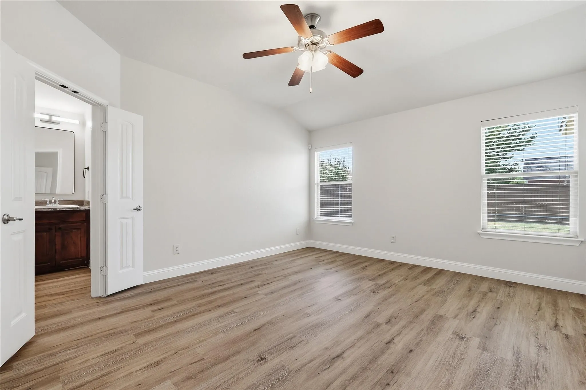 Vaulted ceiling with a ceiling fan, wood-finish flooring, two windows with blinds, and white double doors