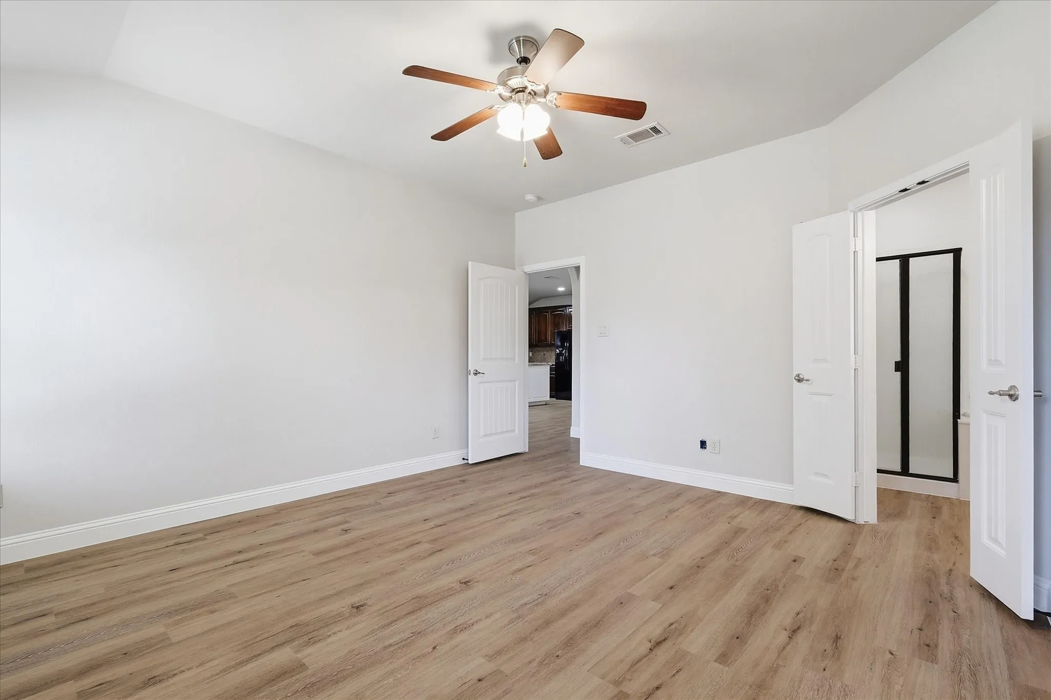 Spacious room featuring wood-finish flooring, light-colored walls, and a ceiling fan