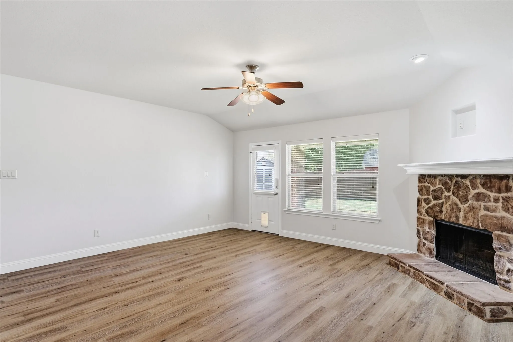 Wood-finish flooring throughout, ceiling fan with light fixture, stone-faced fireplace with hearth, recessed lighting, and multiple windows