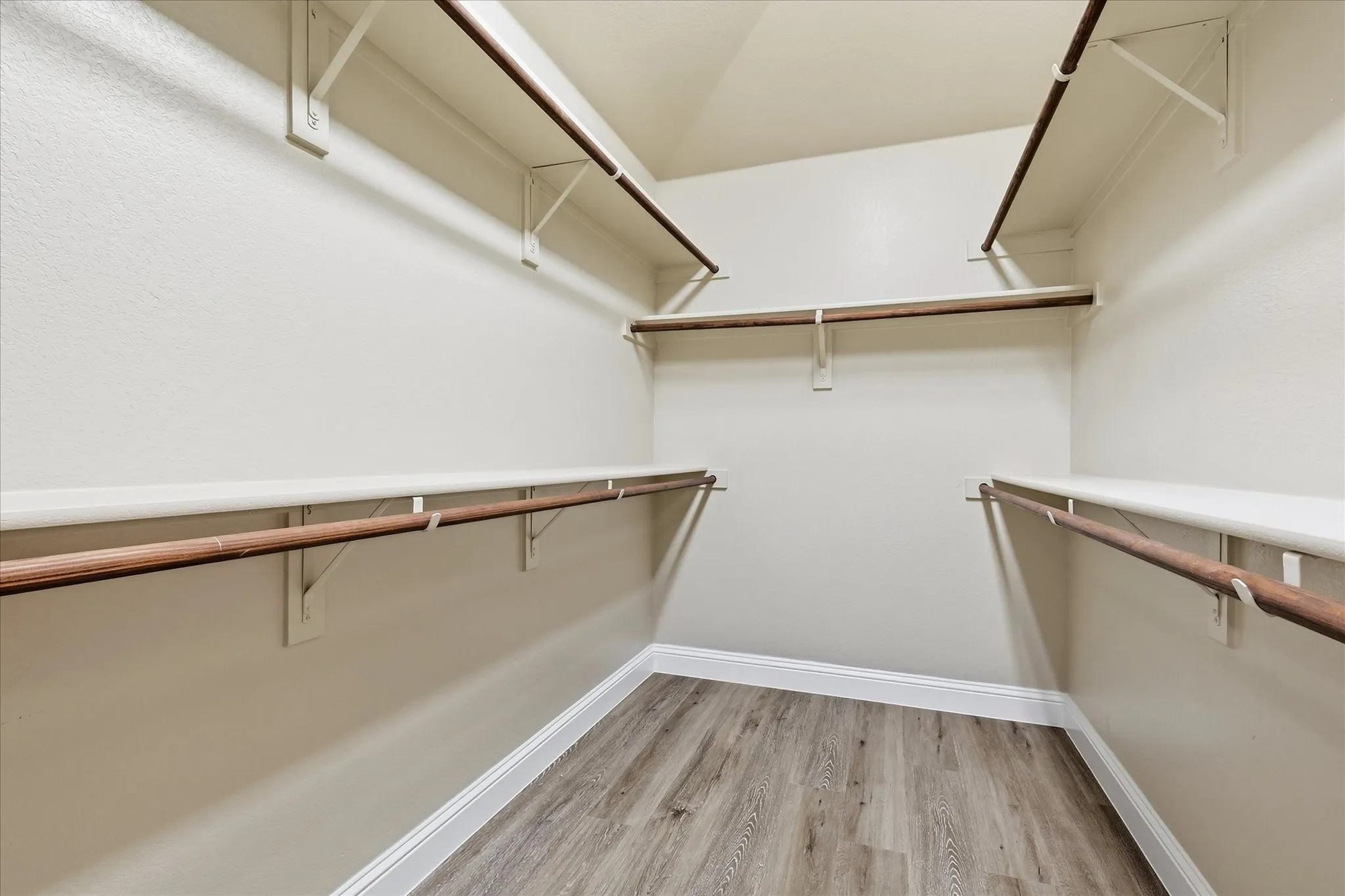 Expansive walk-in closet featuring multiple shelving units, integrated hanging rods, and wood-finish flooring