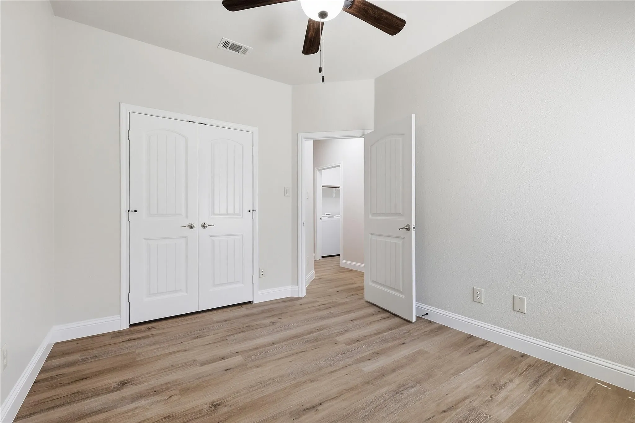 Wood-finish flooring, white paneled doors, ceiling fan, and neutral wall tones