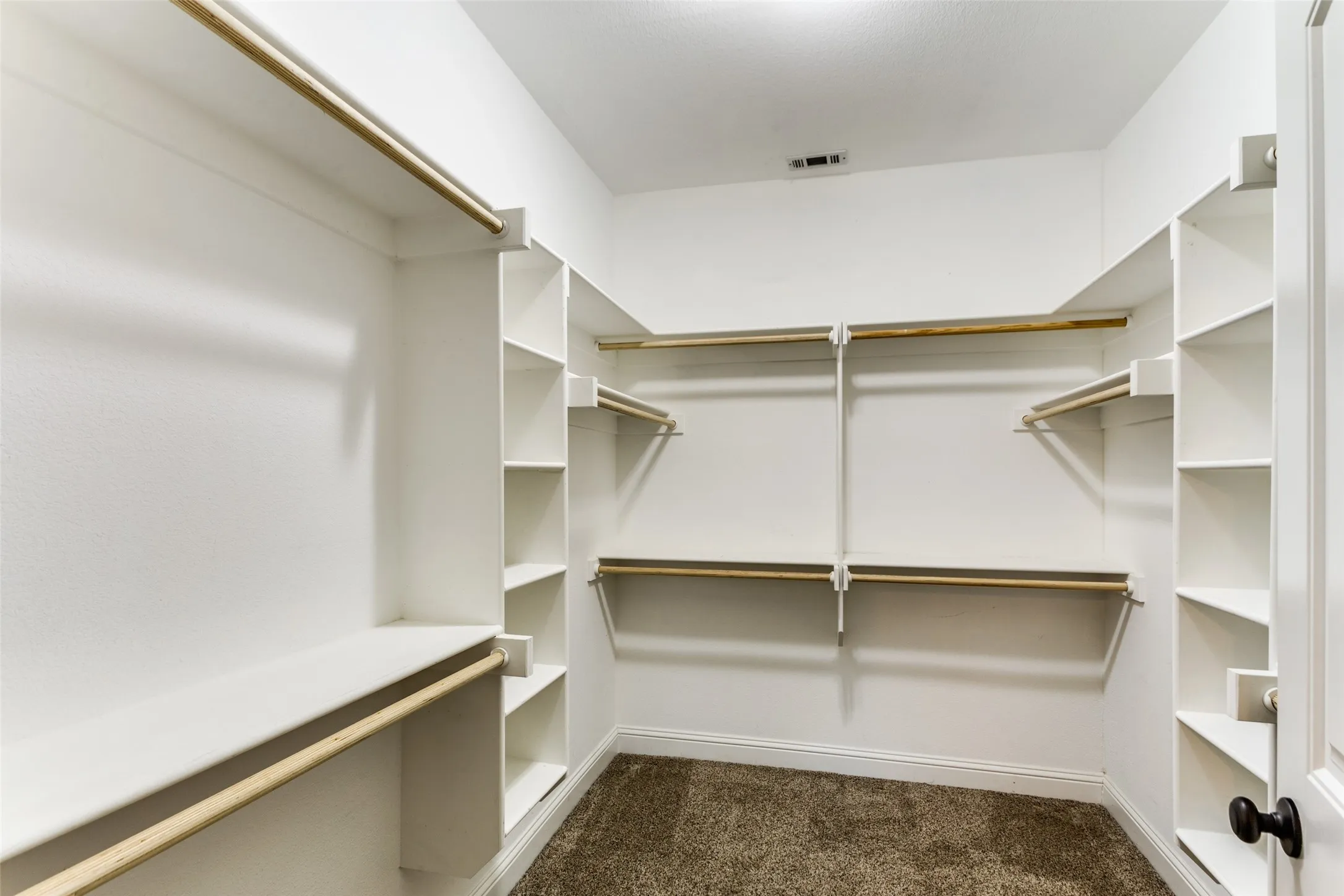 Walk-in closet featuring white built-in shelving, multiple hanging rods, and carpet flooring