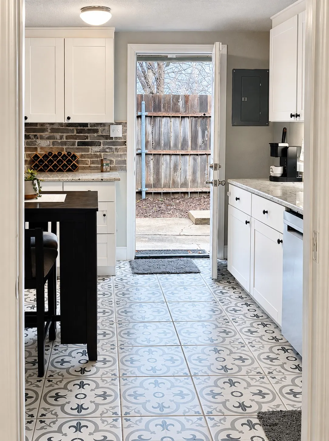 White cabinetry with black hardware, stone countertops, brick-style backsplash, patterned tile flooring, and a built-in kitchen island
