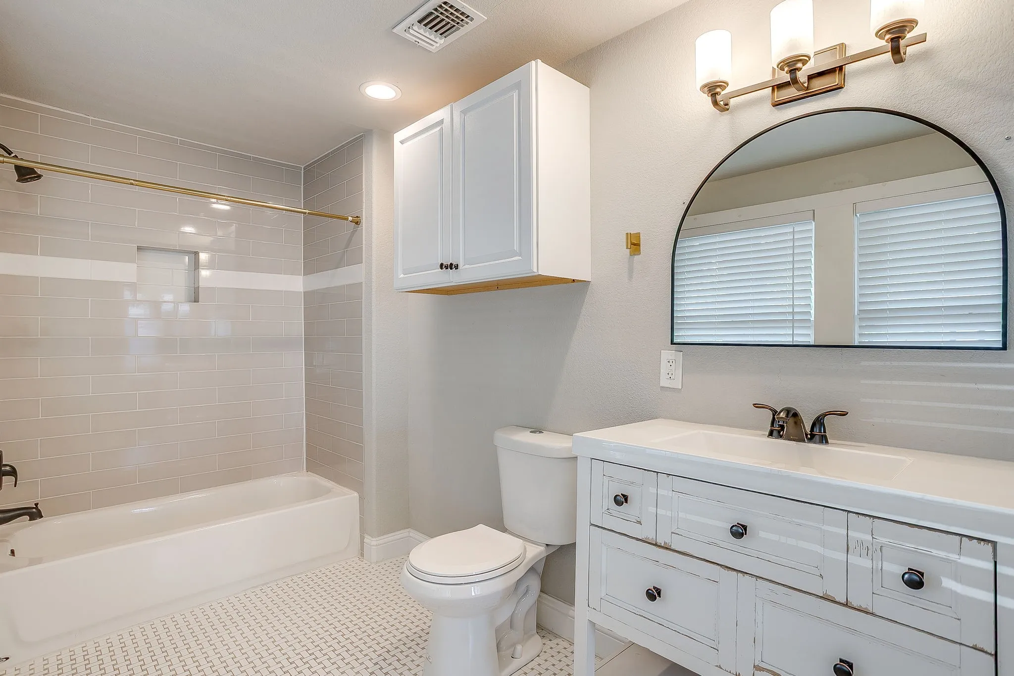 White vanity with integrated sink, arched mirror, contemporary wall sconce, and wall-mounted cabinetry