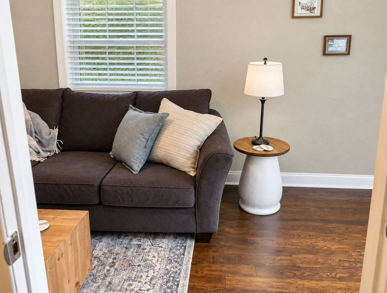 Wood-finish flooring with white trim, light-toned wall paint, and a window with white blinds