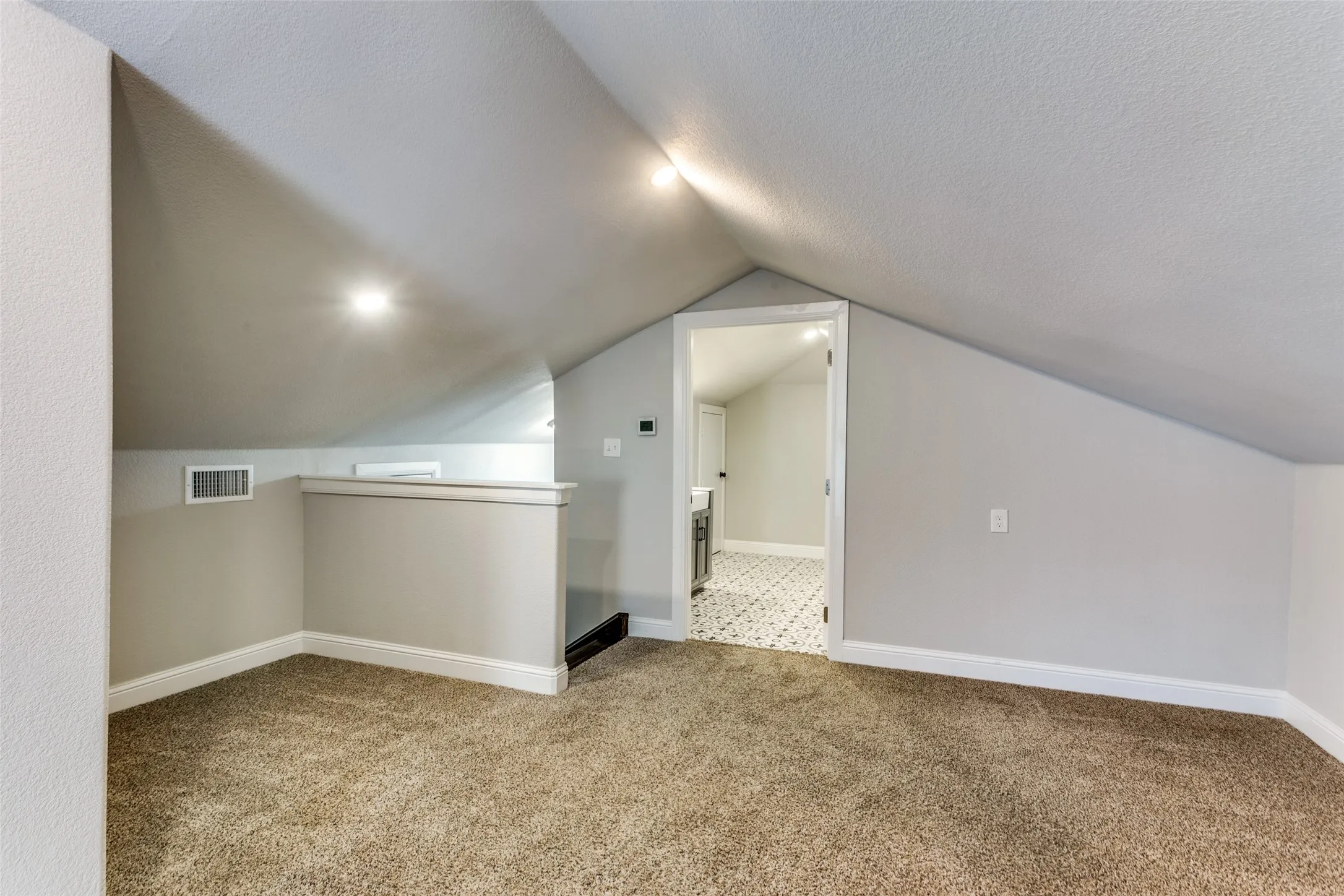 Carpeted flooring, sloped ceilings, recessed lighting, and a doorway to an area with patterned tile flooring
