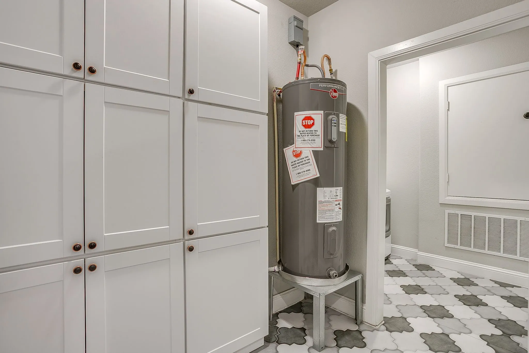 White shaker-style cabinetry with bronze hardware, water heater, and multi-tone geometric tile flooring