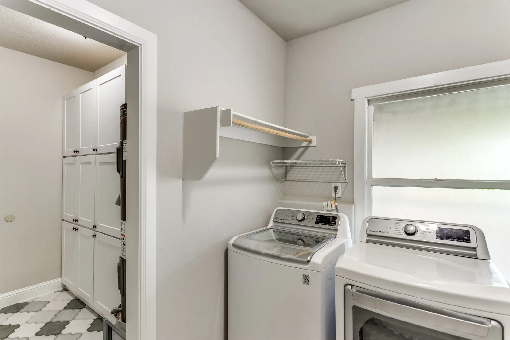 Built-in shelving, white cabinetry with dark hardware, pattern tile flooring, and a window for natural light