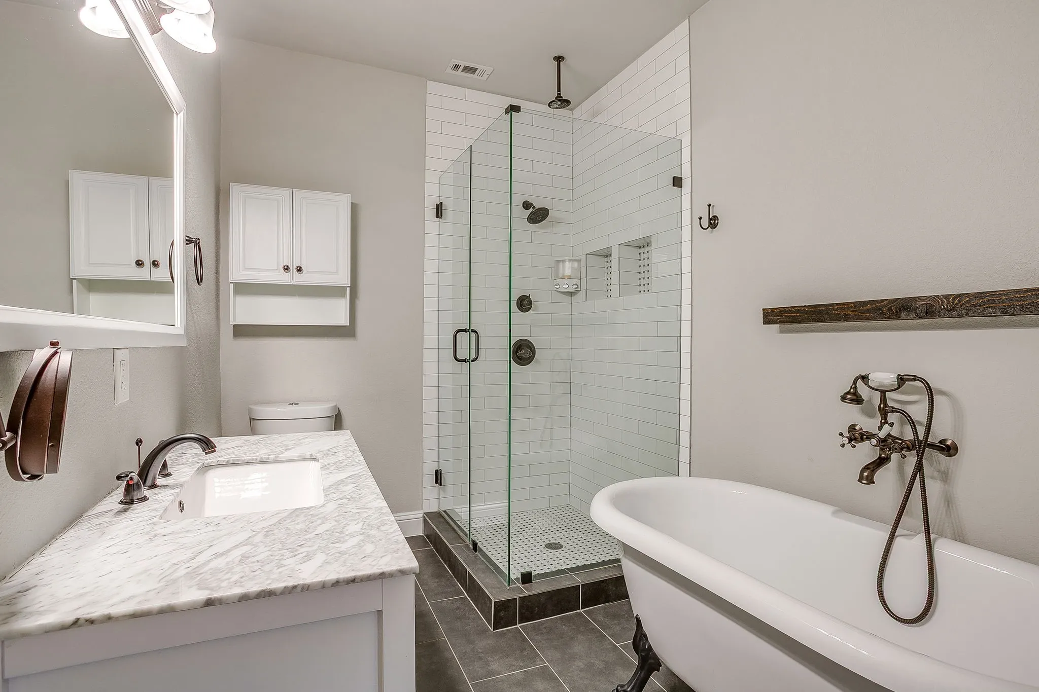 Freestanding claw-foot tub, glass-enclosed shower with subway tile, built-in shower niche, and a vanity with a stone countertop