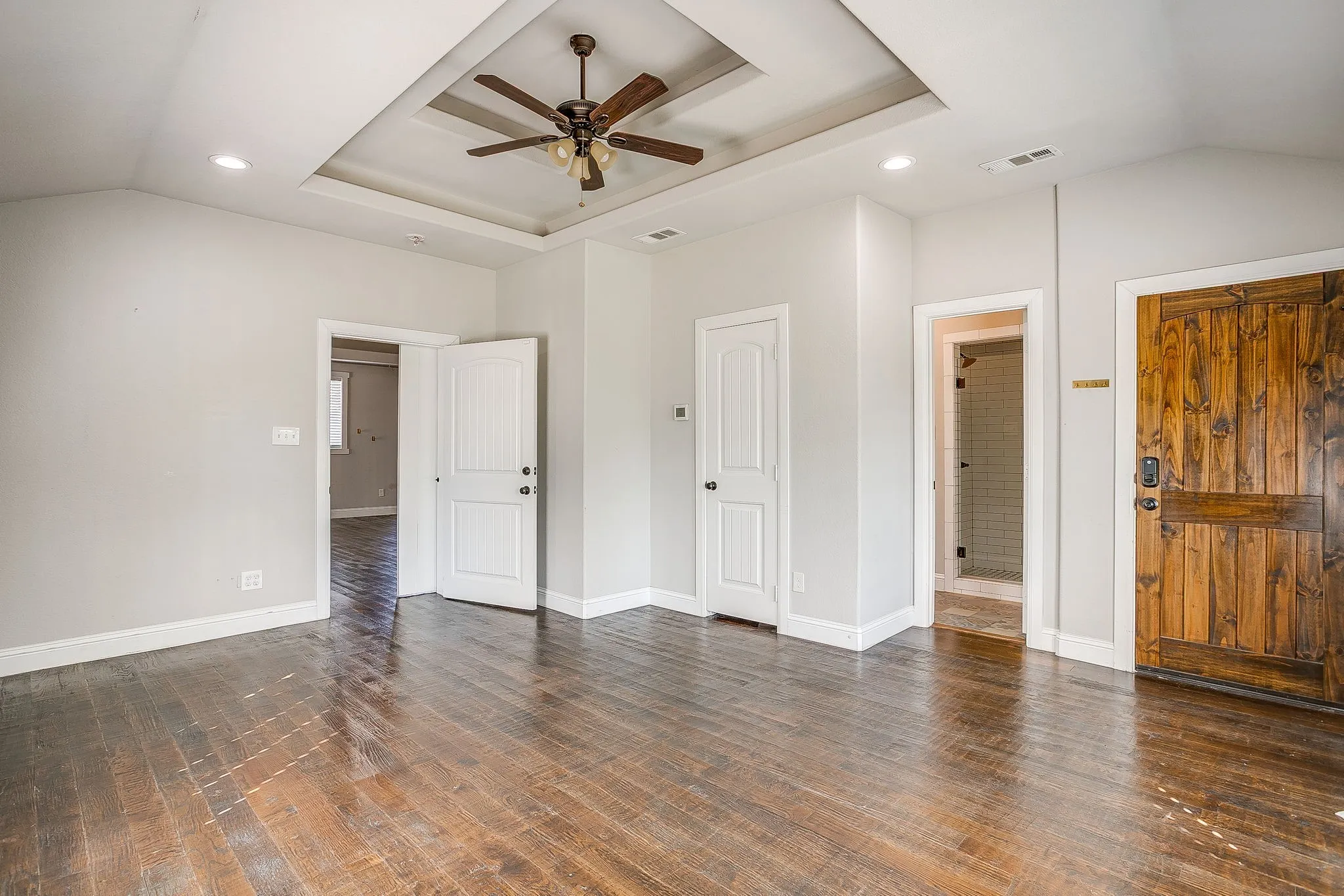 Tray ceiling with a ceiling fan, recessed lighting, wood-finish flooring, and a unique wood plank door