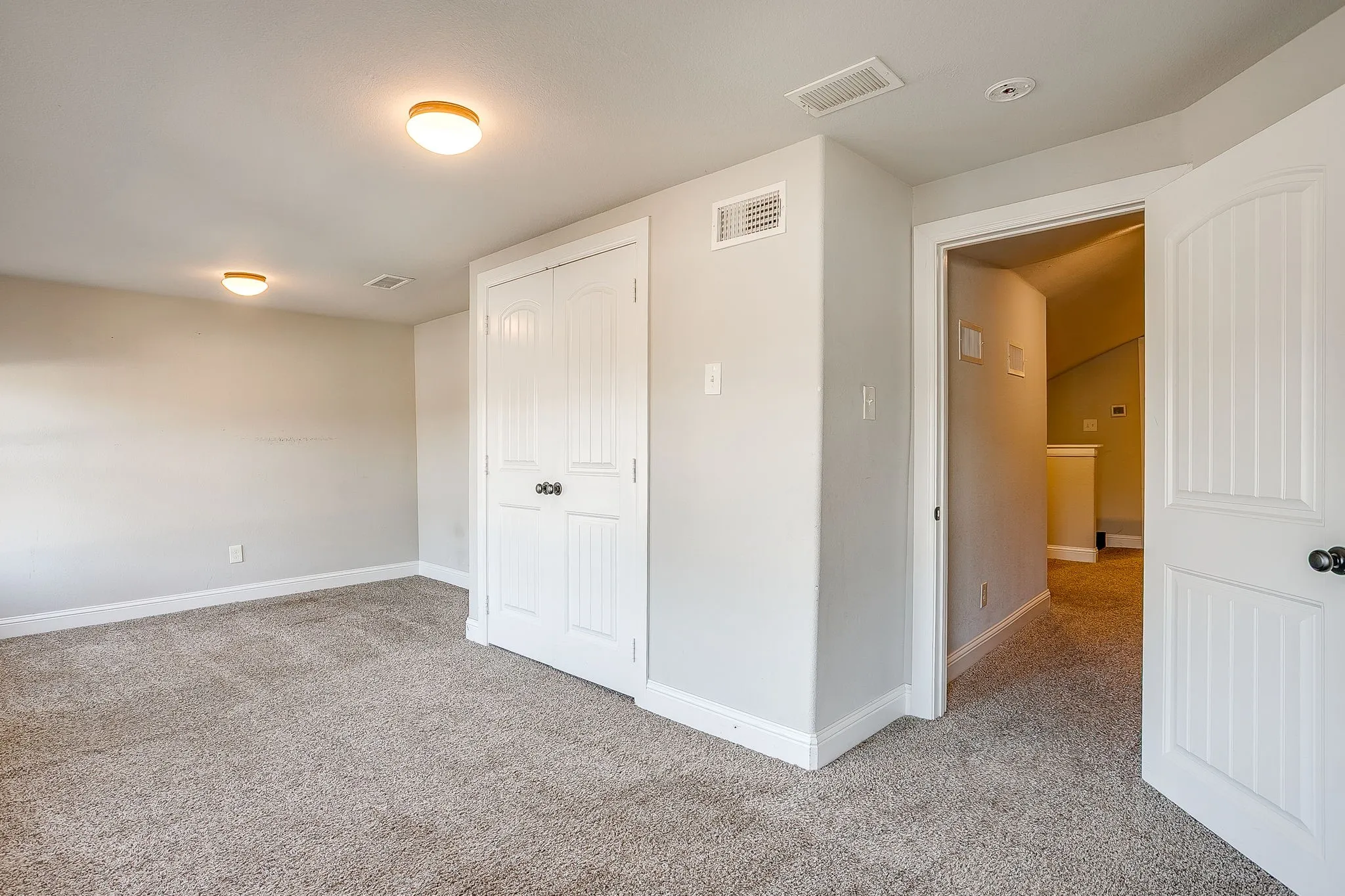 Light gray wall paint, textured carpet flooring, white paneled bifold closet doors, white paneled interior door, and flush-mount ceiling lights