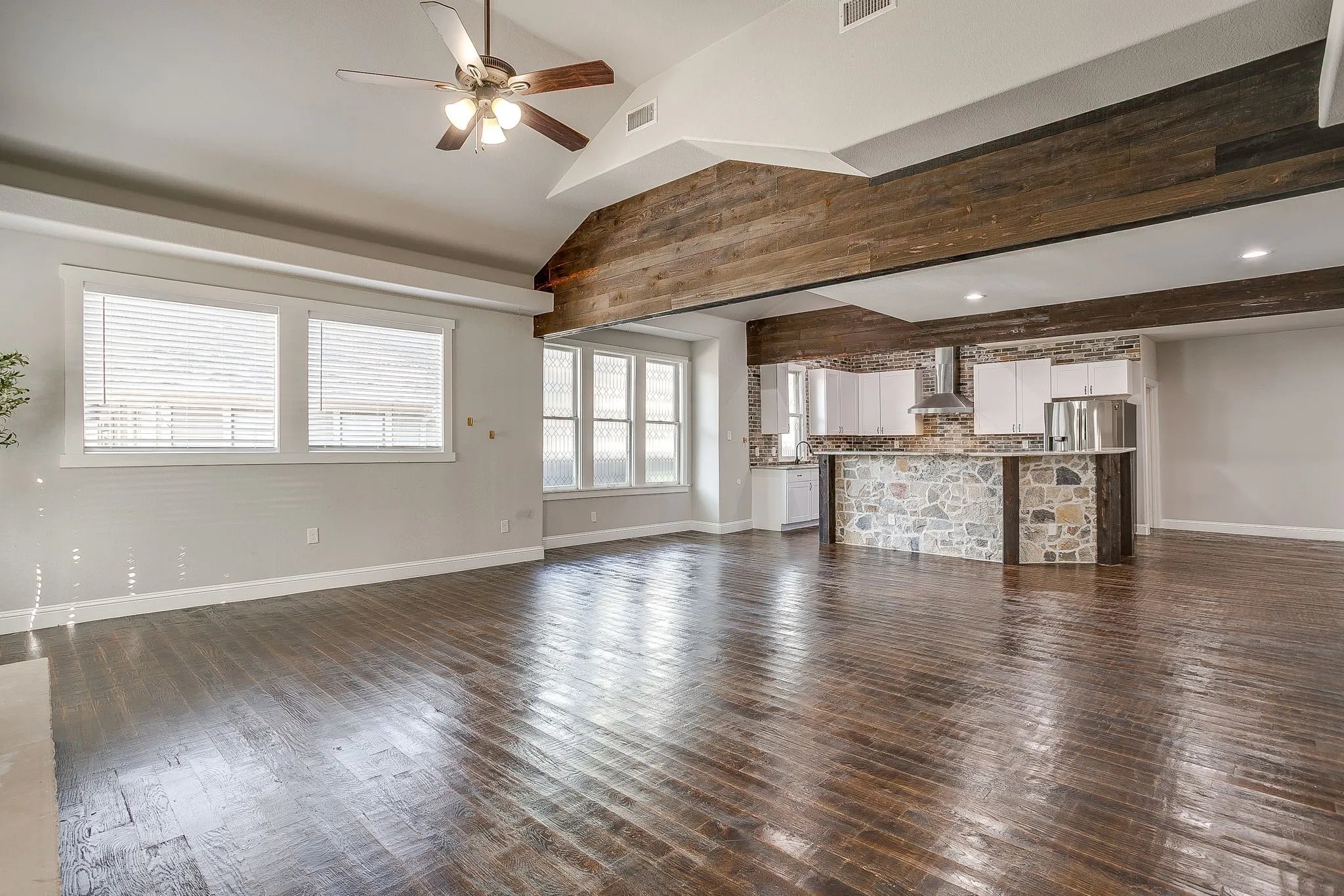 Vaulted ceiling with a ceiling fan, wood-finish flooring, exposed wood beams, and a kitchen featuring white cabinetry and stone-clad island