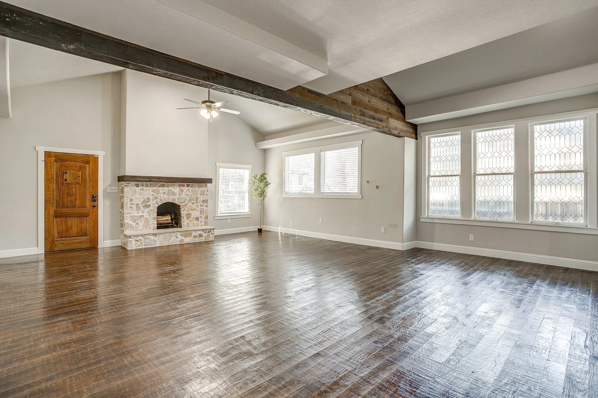 Vaulted ceilings with exposed wood beams, stone-clad fireplace with wood mantle, wood-finish flooring, and decorative windowpanes