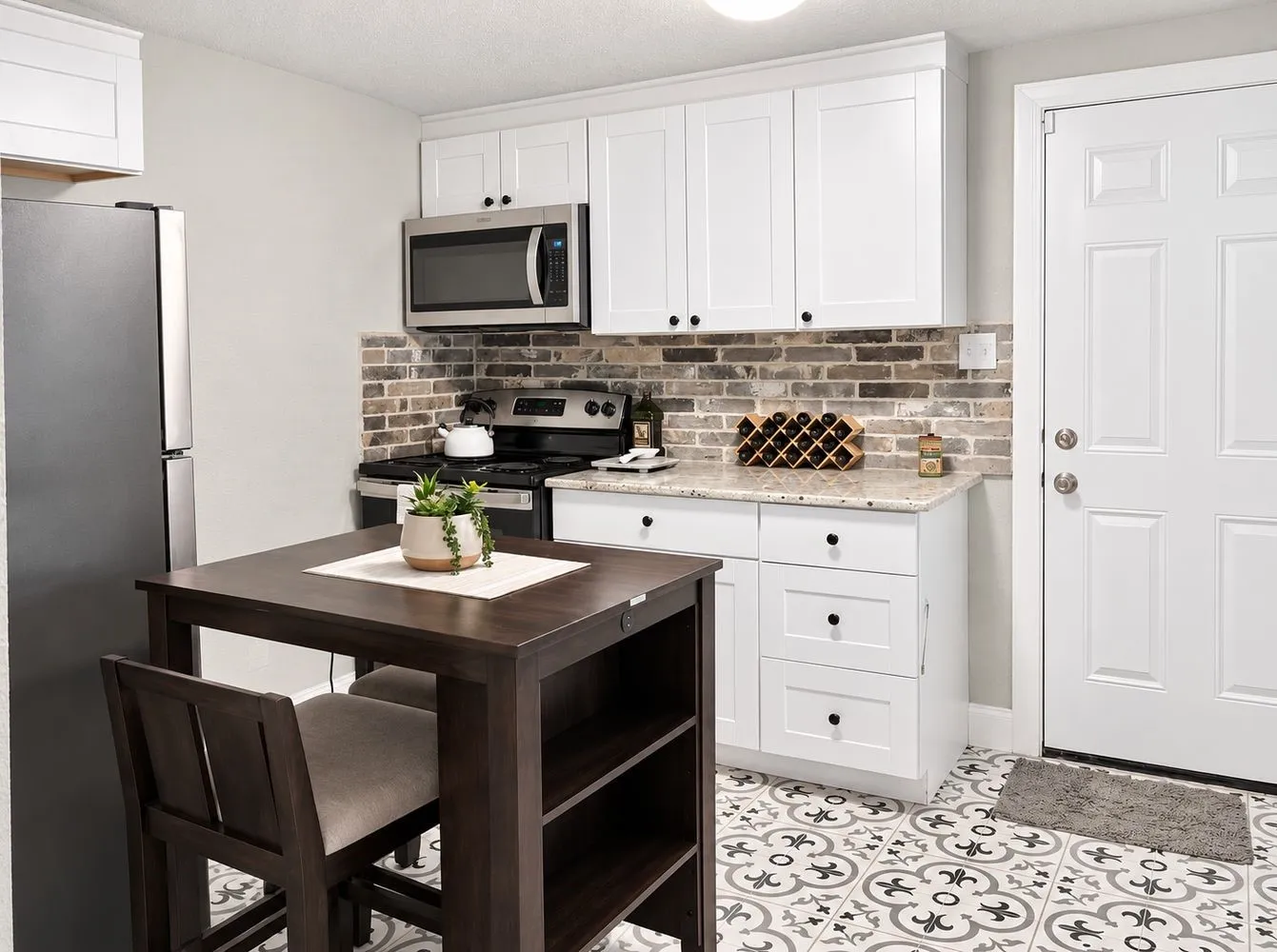 White shaker cabinetry, stainless steel appliances, brick-patterned tile backsplash, light-toned countertops, and patterned floor tiling