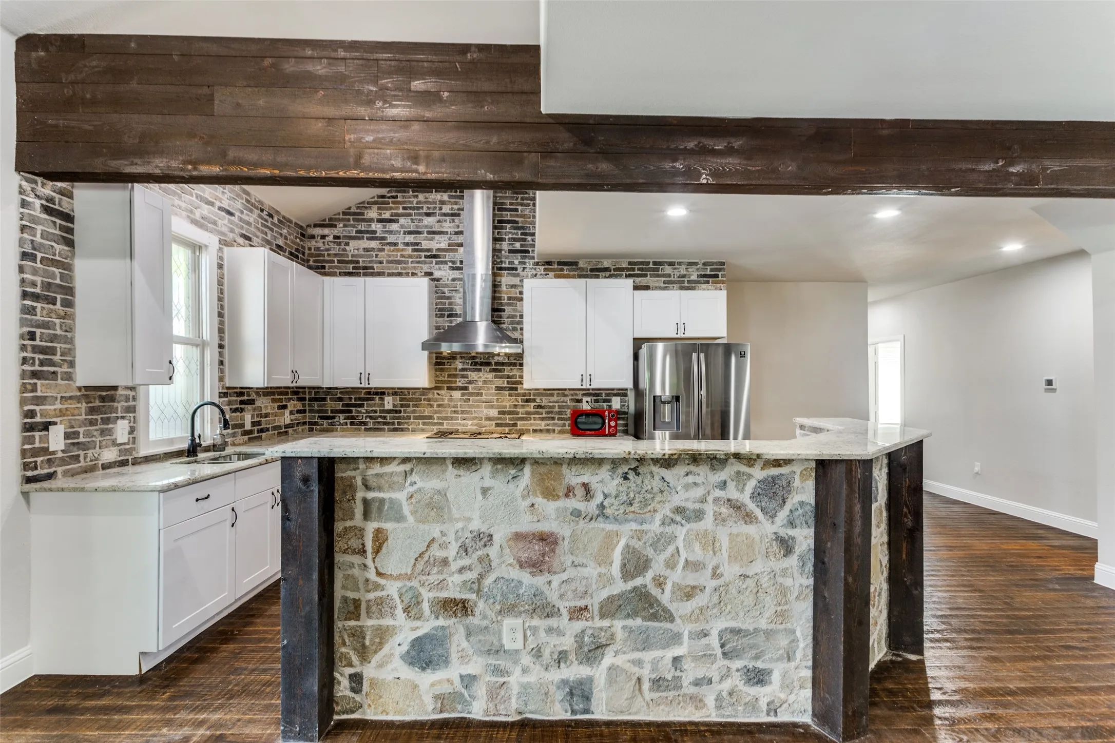Kitchen featuring a stone-clad breakfast bar, wood-finish flooring, white cabinetry, integrated stainless steel appliances, and brick-style backsplash