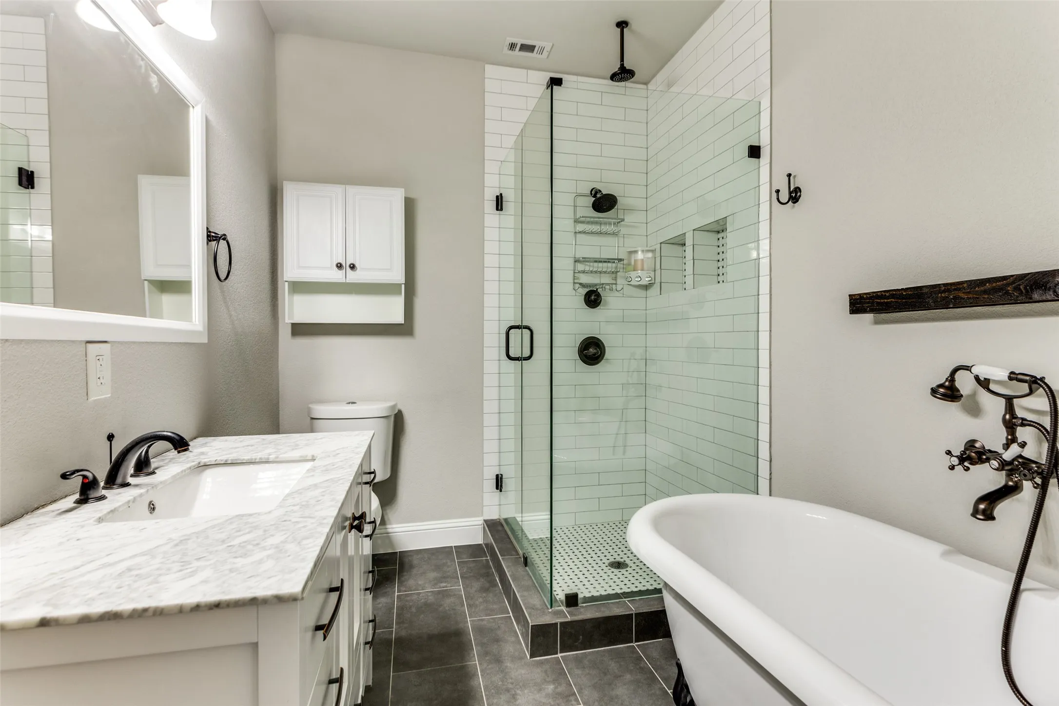 White vanity with a stone countertop, a walk-in shower featuring subway tile, a freestanding bathtub, and dark-finish fixtures