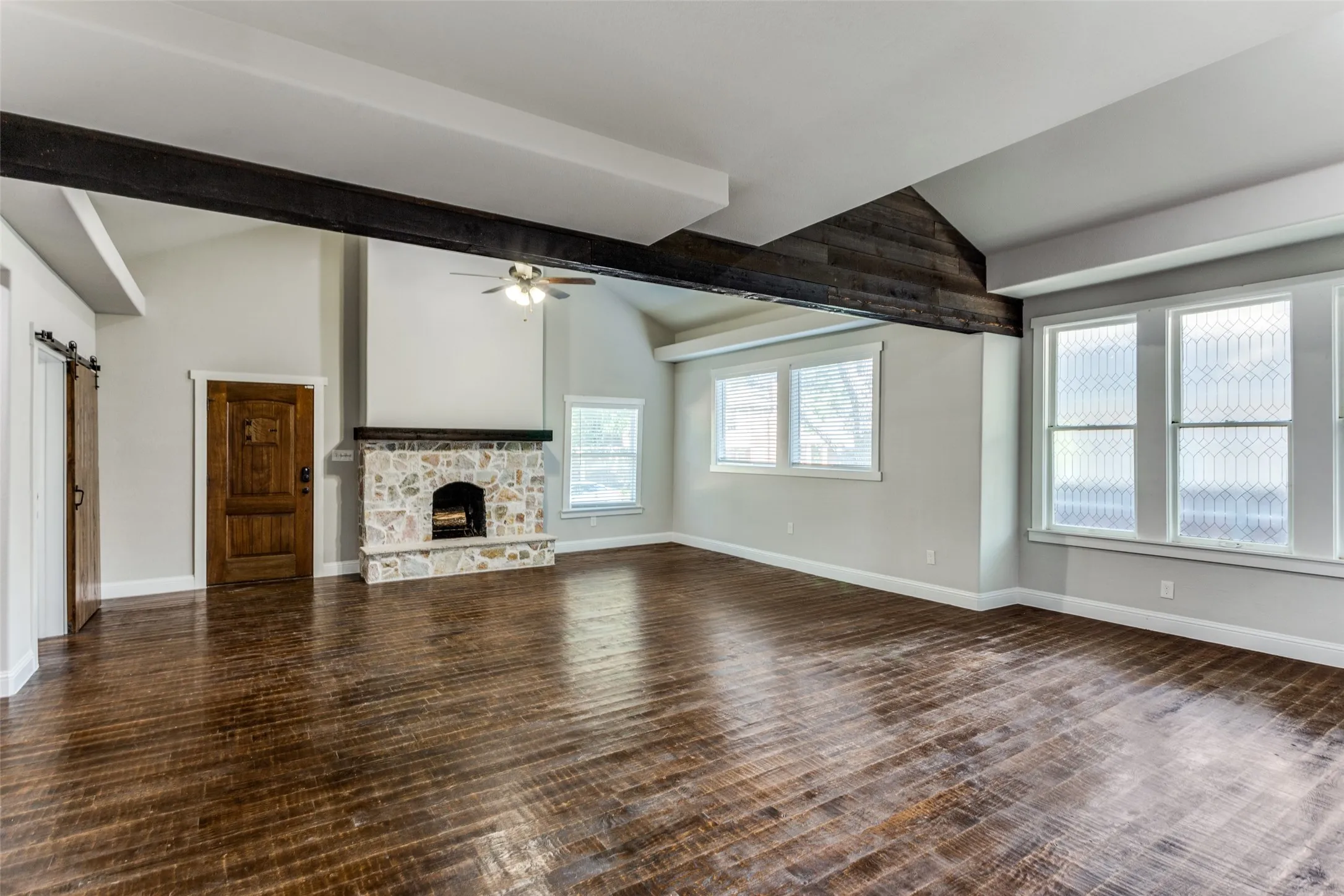 Vaulted ceiling with exposed beam accents, wood-finish flooring, stone fireplace, and multiple windows