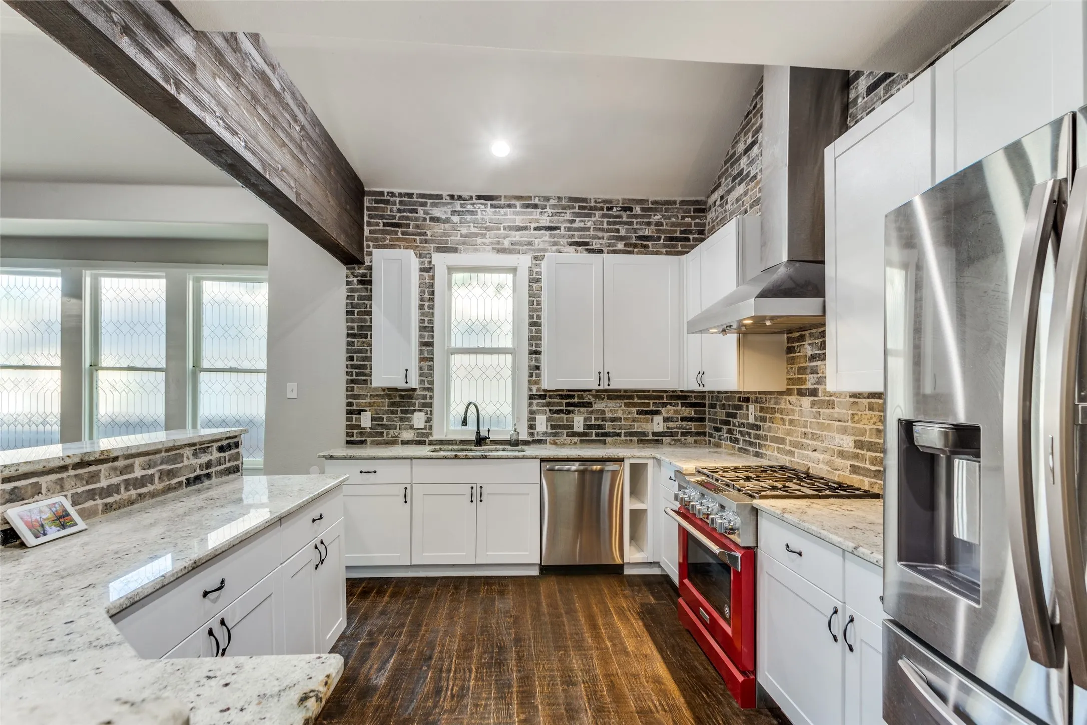 Kitchen featuring white cabinetry, light-toned countertops, a brick-patterned backsplash, stainless steel appliances, and wood-finish flooring